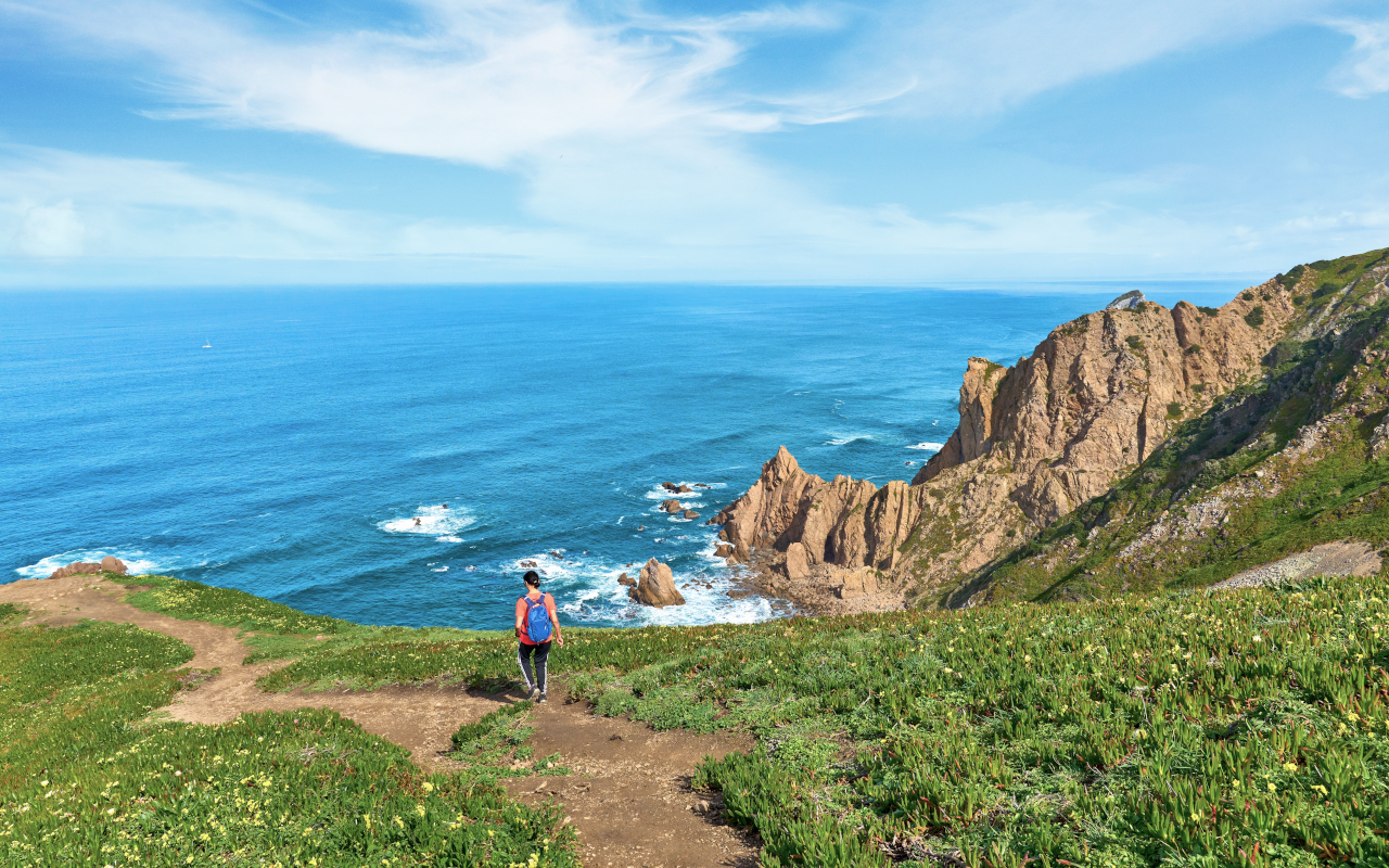 Persona caminando por los acantilados verdes con vistas al océano en Cabo da Roca.
