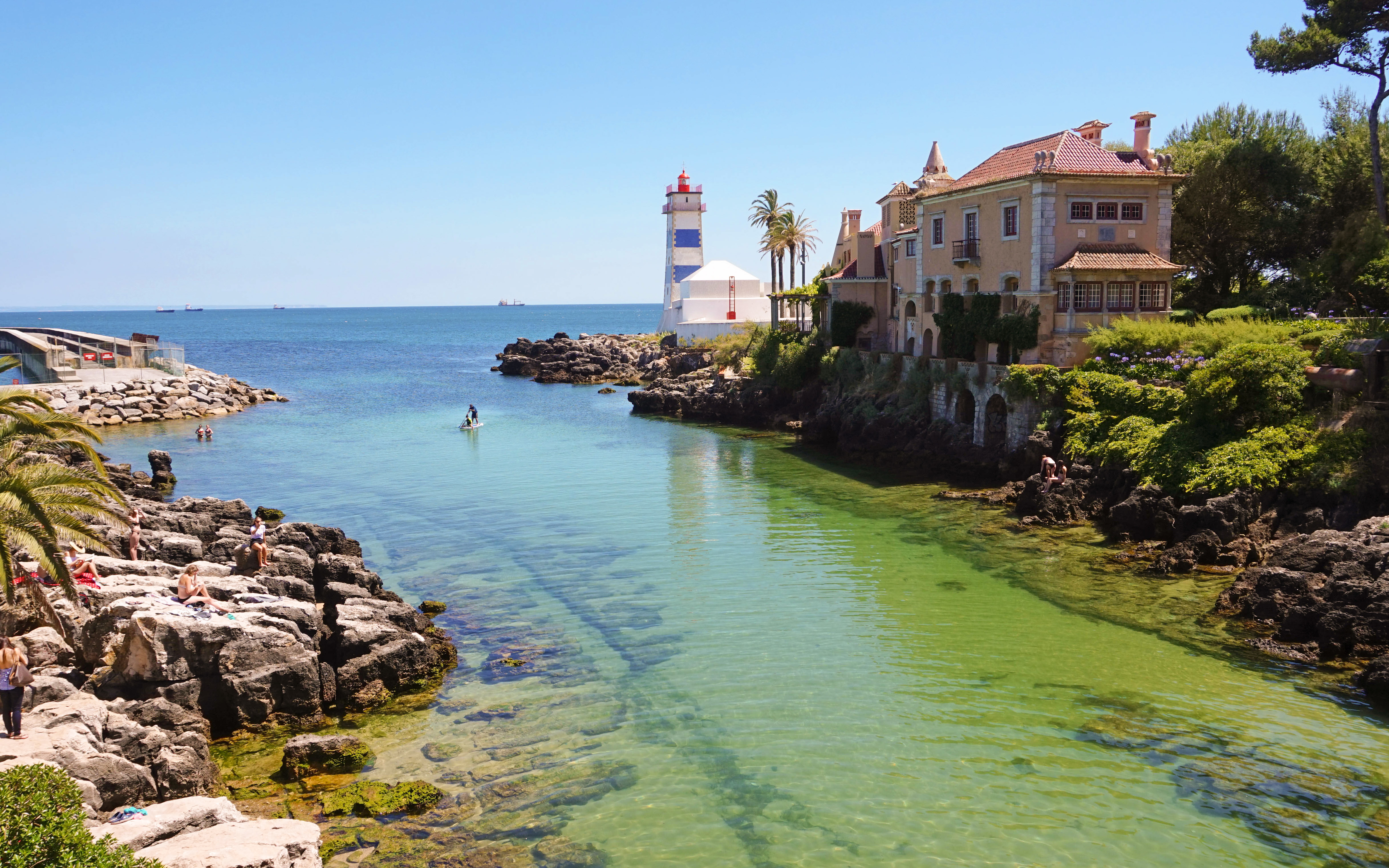 Cala de Cascais con aguas turquesas, casas costeras y faro al fondo.