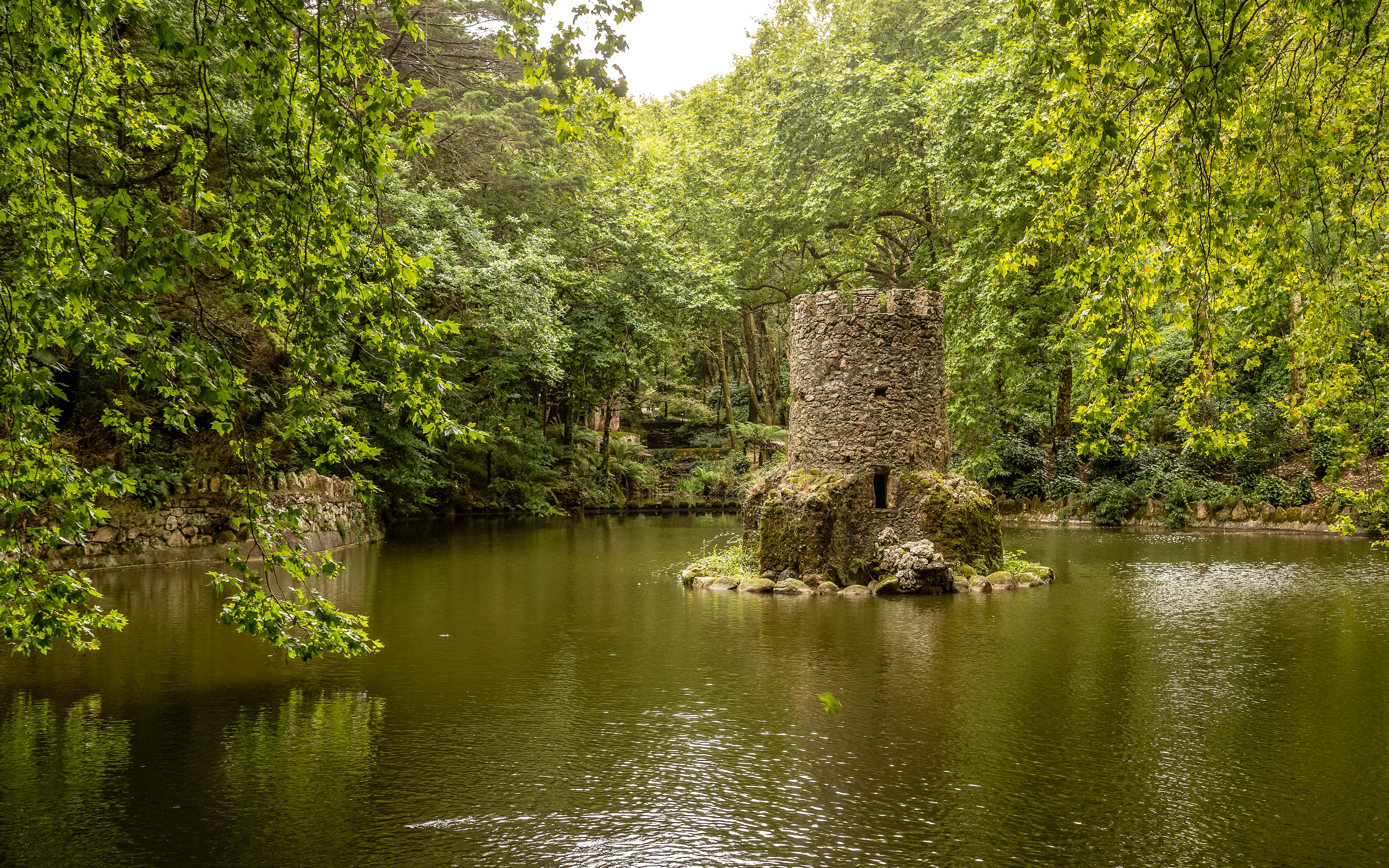 Torre de piedra en un lago rodeado de frondoso bosque en los jardines de Sintra.