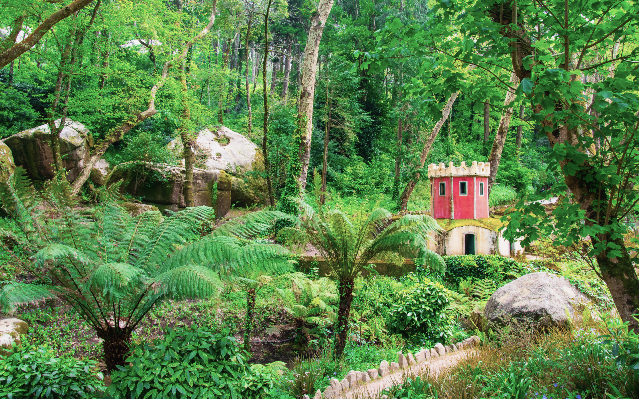 Jardines del Palacio da Pena con vegetación frondosa y una pequeña torre roja.