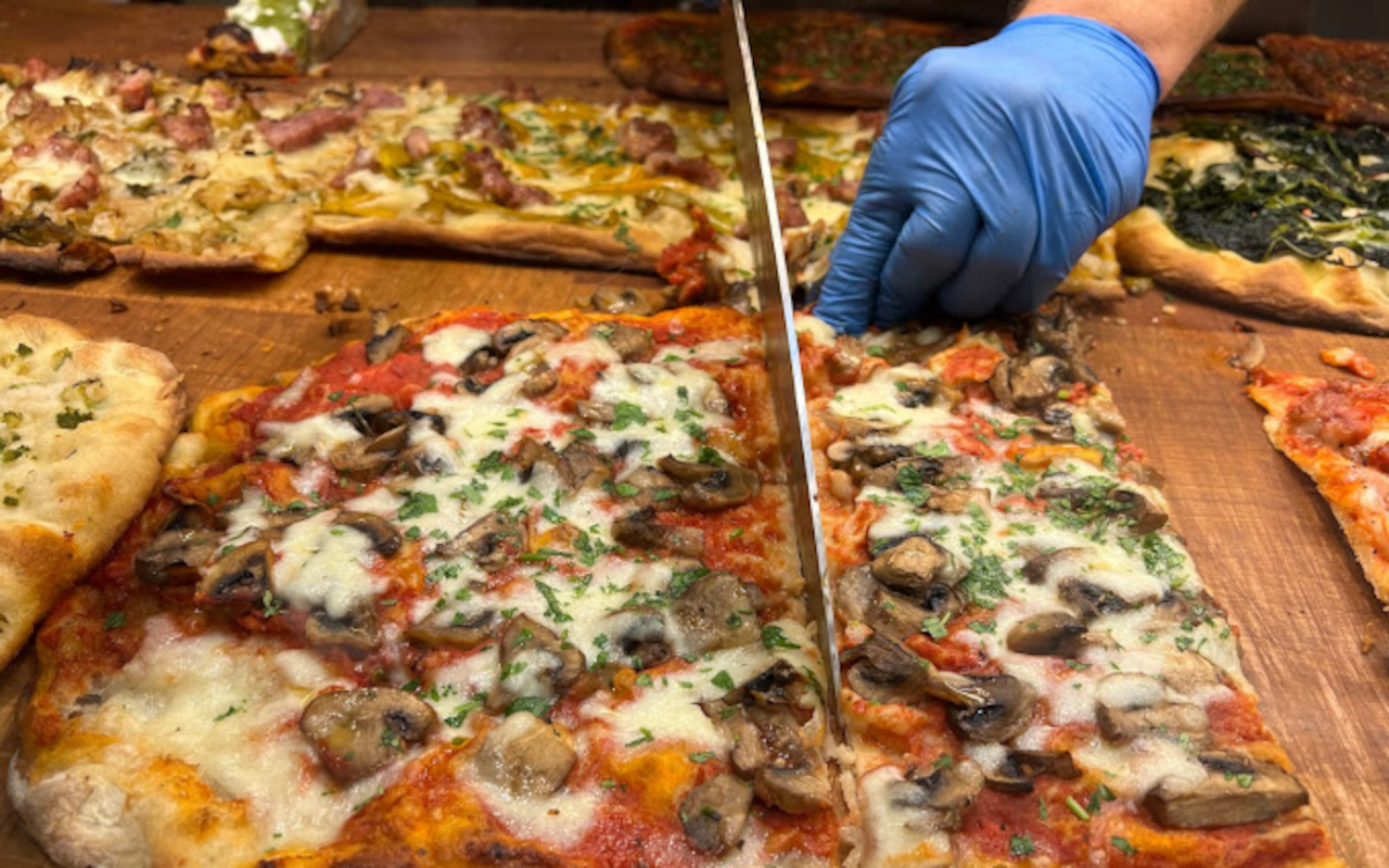 Pizzero italiano cortando una pizza con purchetta, otra de las recetas típicas que se prueban en este tour gastronómico por el barrio de Trastevere.