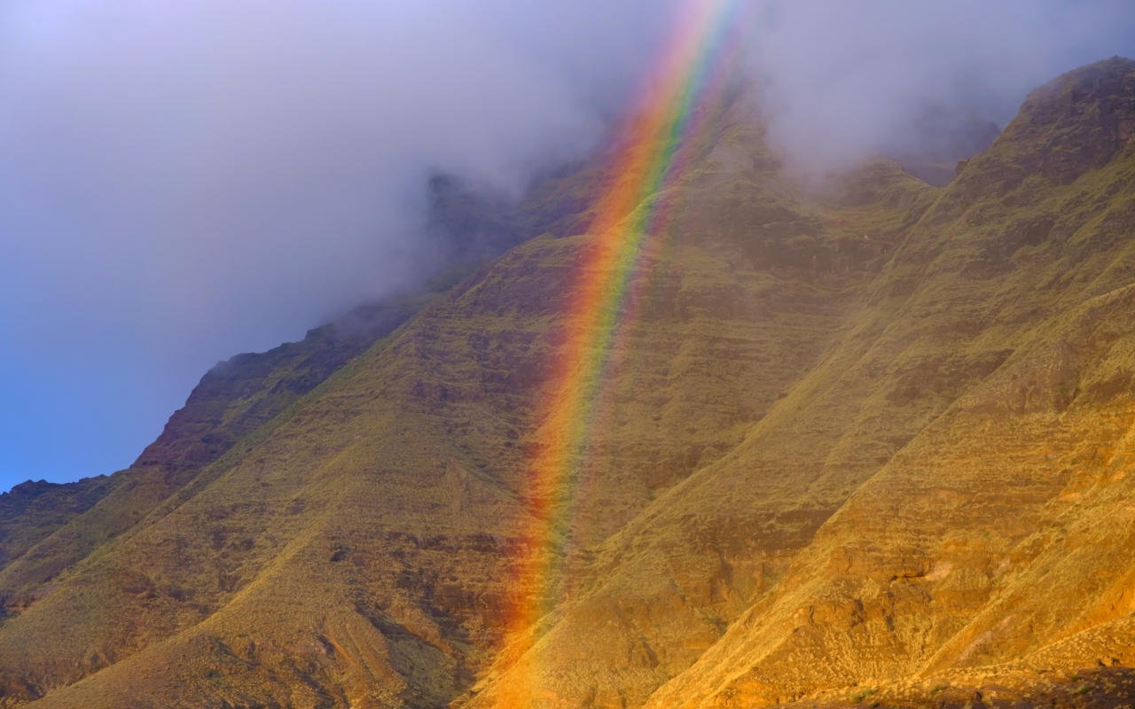 Mountains surrounded by clouds and a rainbow in Tamadaba Natural Park