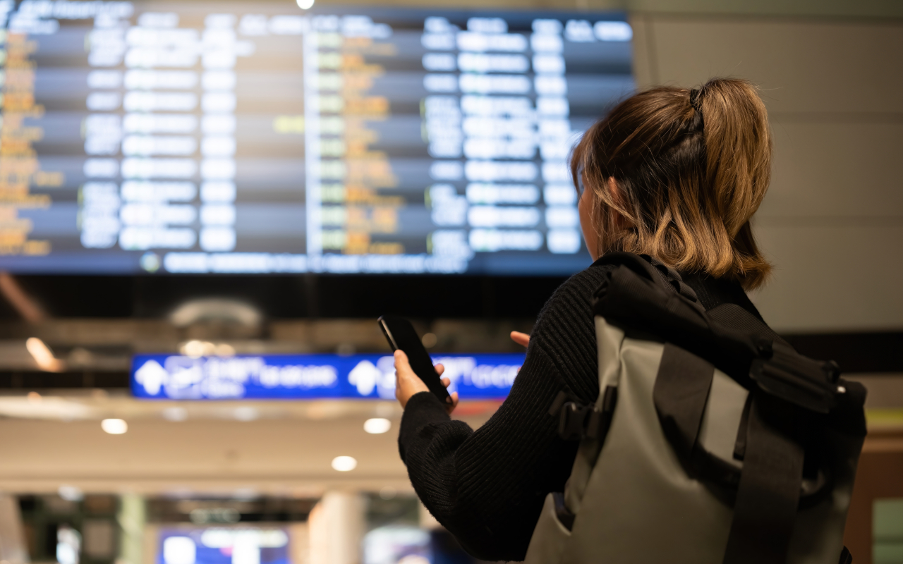 Chica mira una lista de vuelos en el aeropuerto. Si el vuelo sufre algún retraso el chófer lo sabrá.