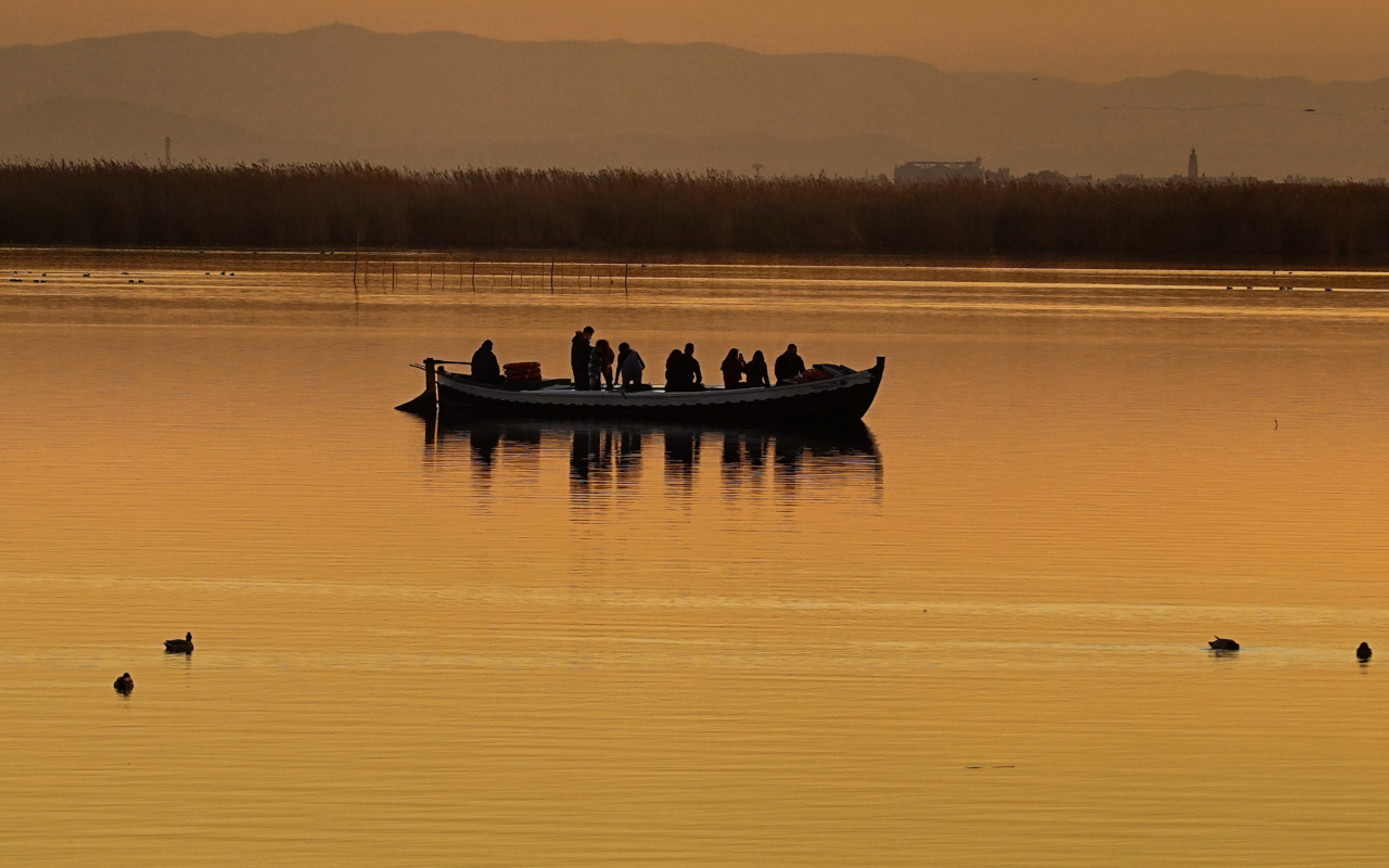 Una barca tradicional cruza el lago mientras el sol se refleja en el agua. 