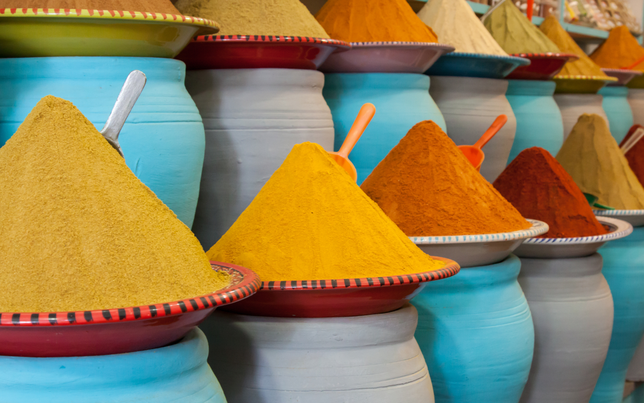 Montículos de especias tradicionales marroquíes en tonos cálidos, dispuestos en mercados locales sobre recipientes de cerámica.