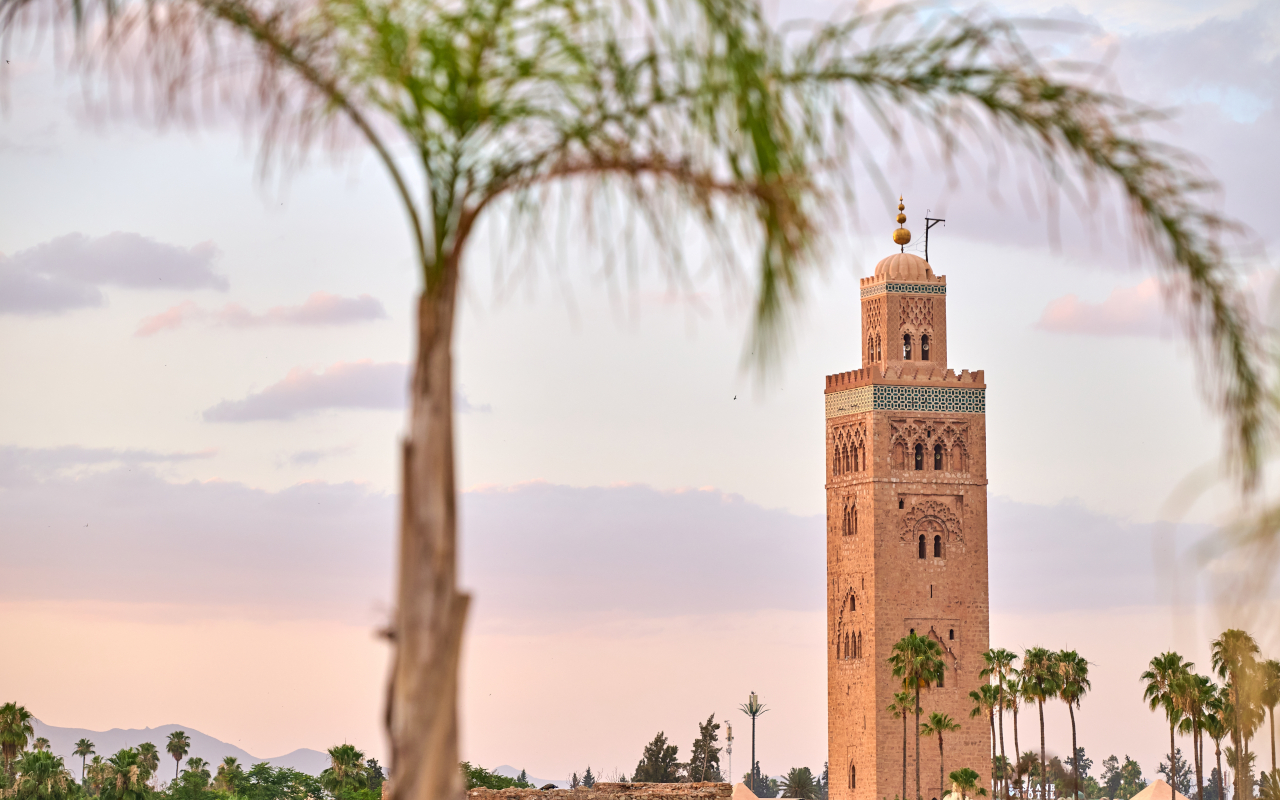 Minarete de la mezquita Koutoubia de Marrakech enmarcado por palmeras al atardecer, símbolo de la ciudad.