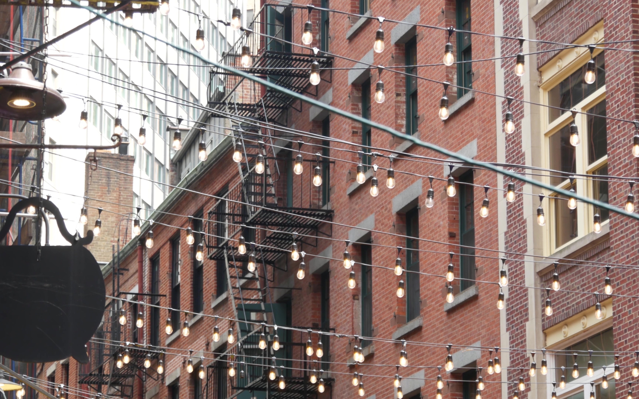Calle Stone Street en Nueva York con luces colgantes y fachadas de ladrillo estilo histórico.