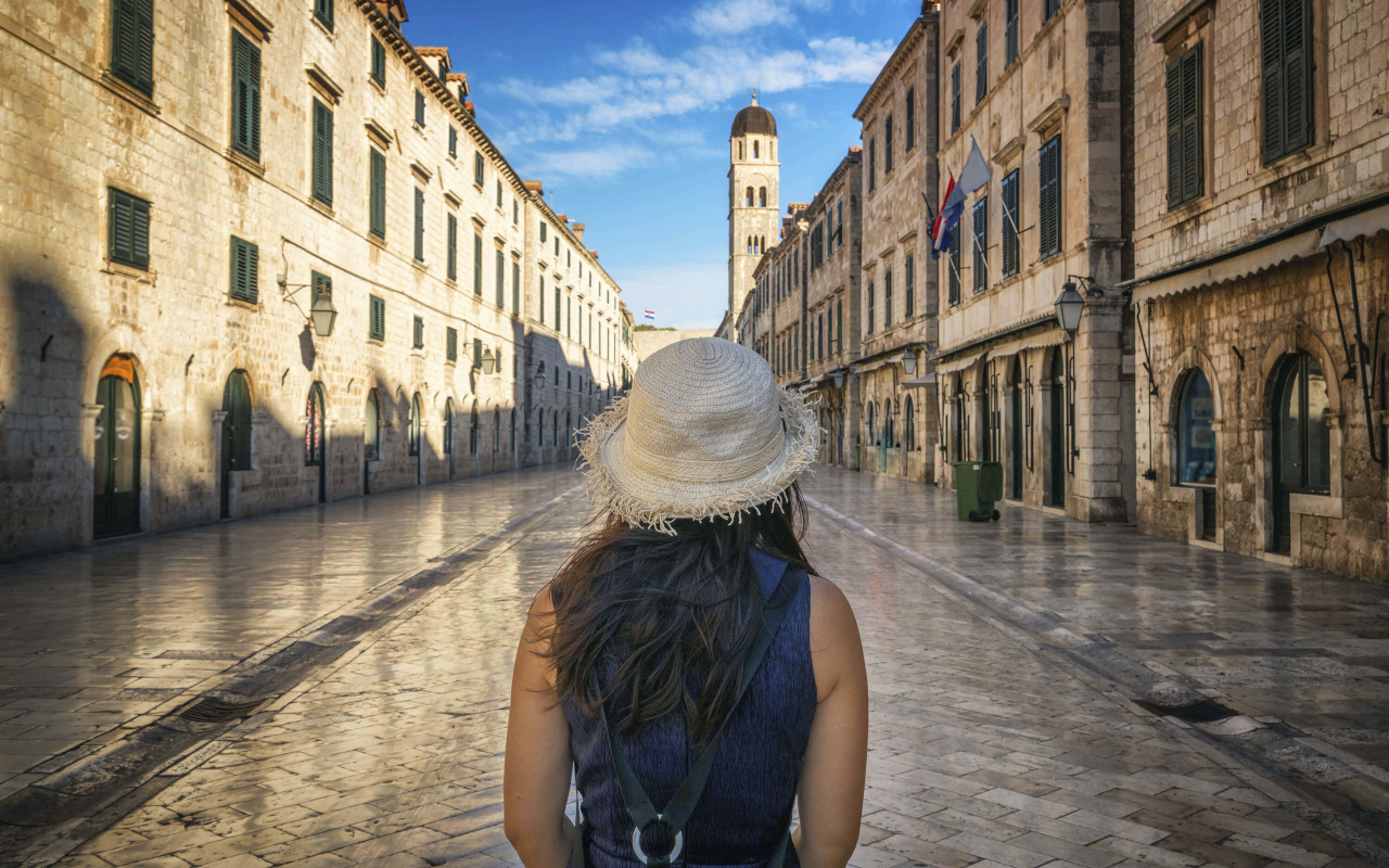 Mujer con sombrero paseando por la calle Stradun de Dubrovnik, al fondo la torre del reloj del casco antiguo.