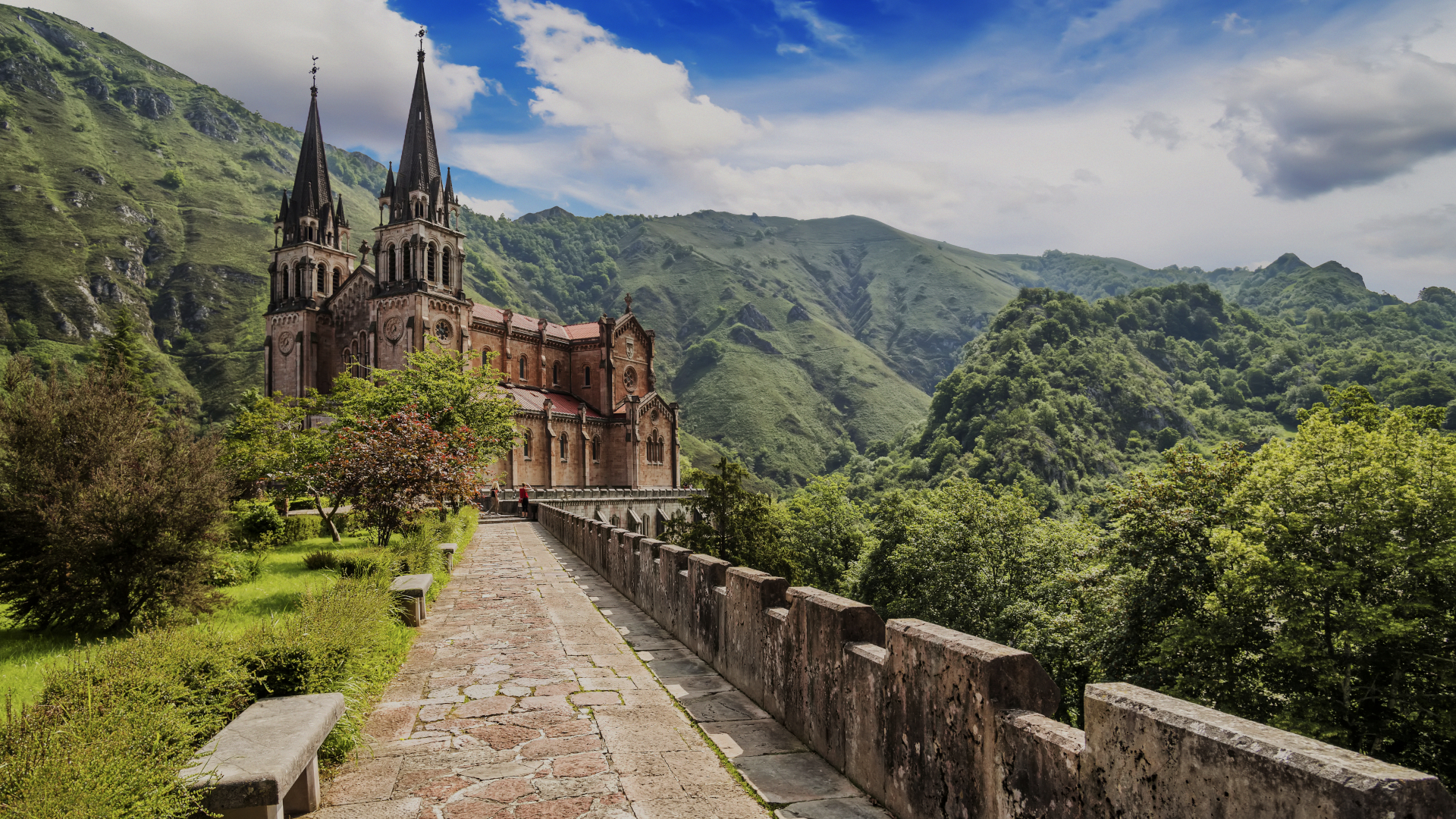 Santuario de Covadonga, Basílica de Santa María la Real, Asturias, rodeado de montañas verdes y cielo azul.