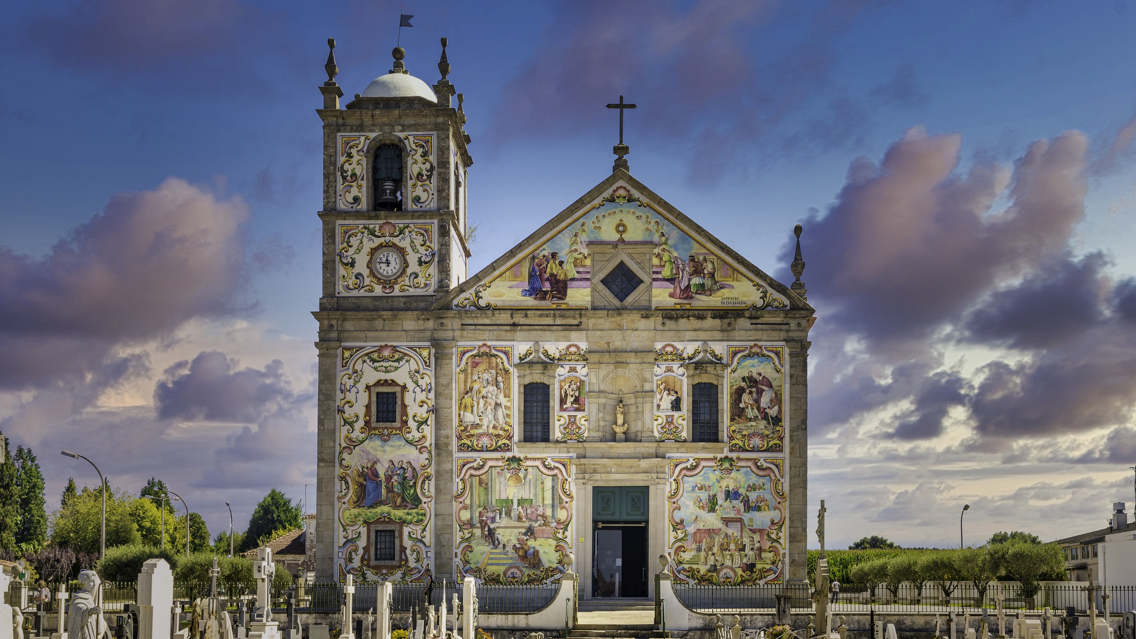 Fachada colorida de la Iglesia de Santa Maria de Válega en Portugal, cubierta con azulejos y campanario lateral.