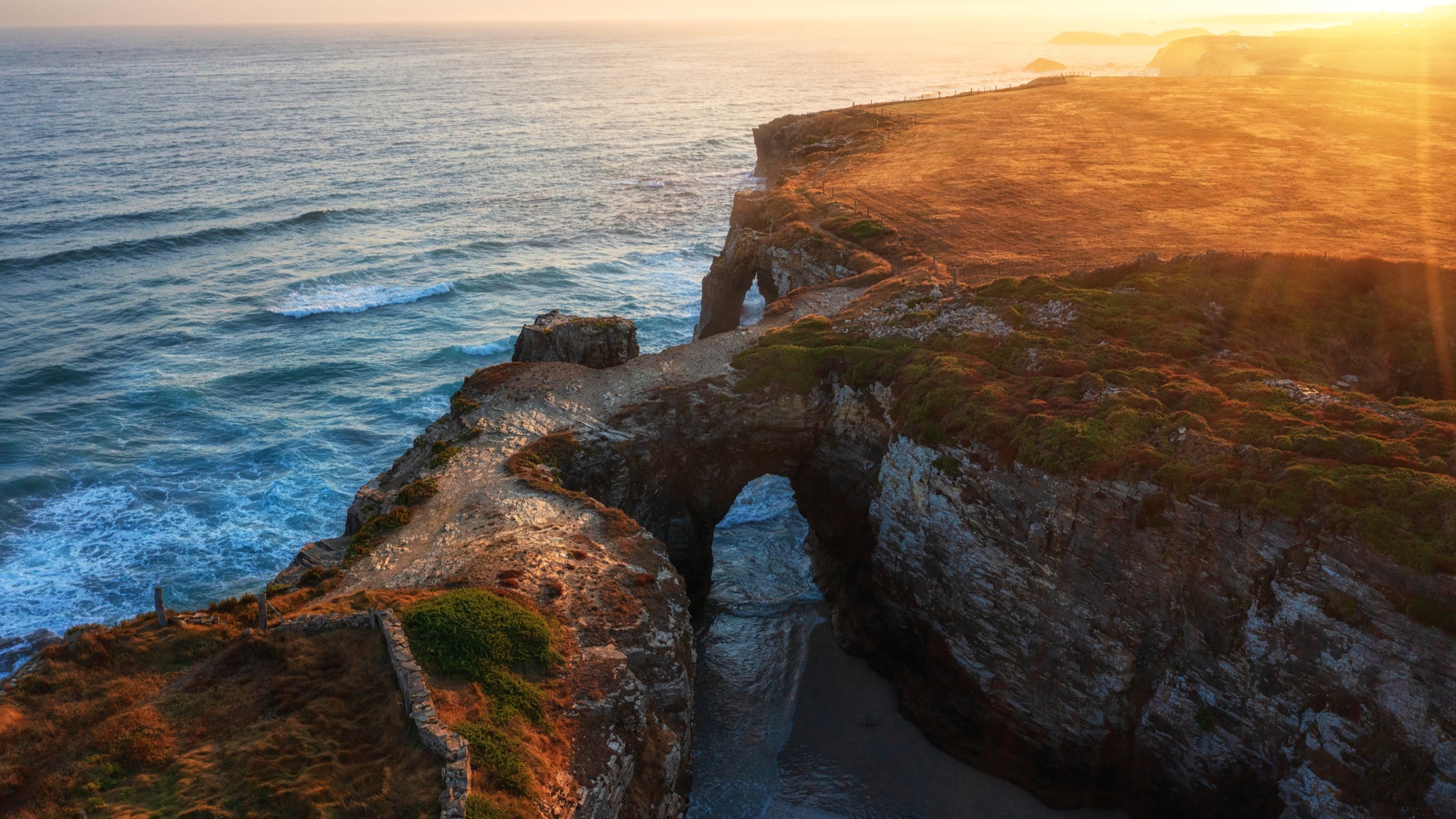 Vista aérea de la Playa de las Catedrales al atardecer, con sus arcos de roca bañados por el mar Cantábrico.