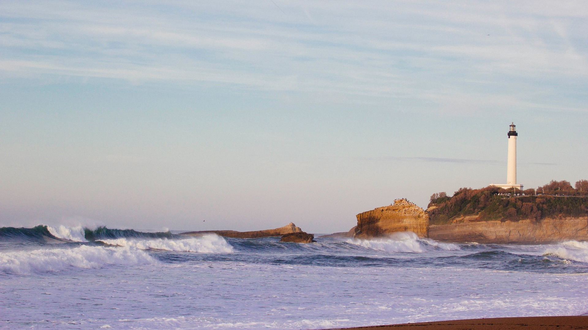 Faro de Biarritz sobre el acantilado con olas rompiendo en la costa.