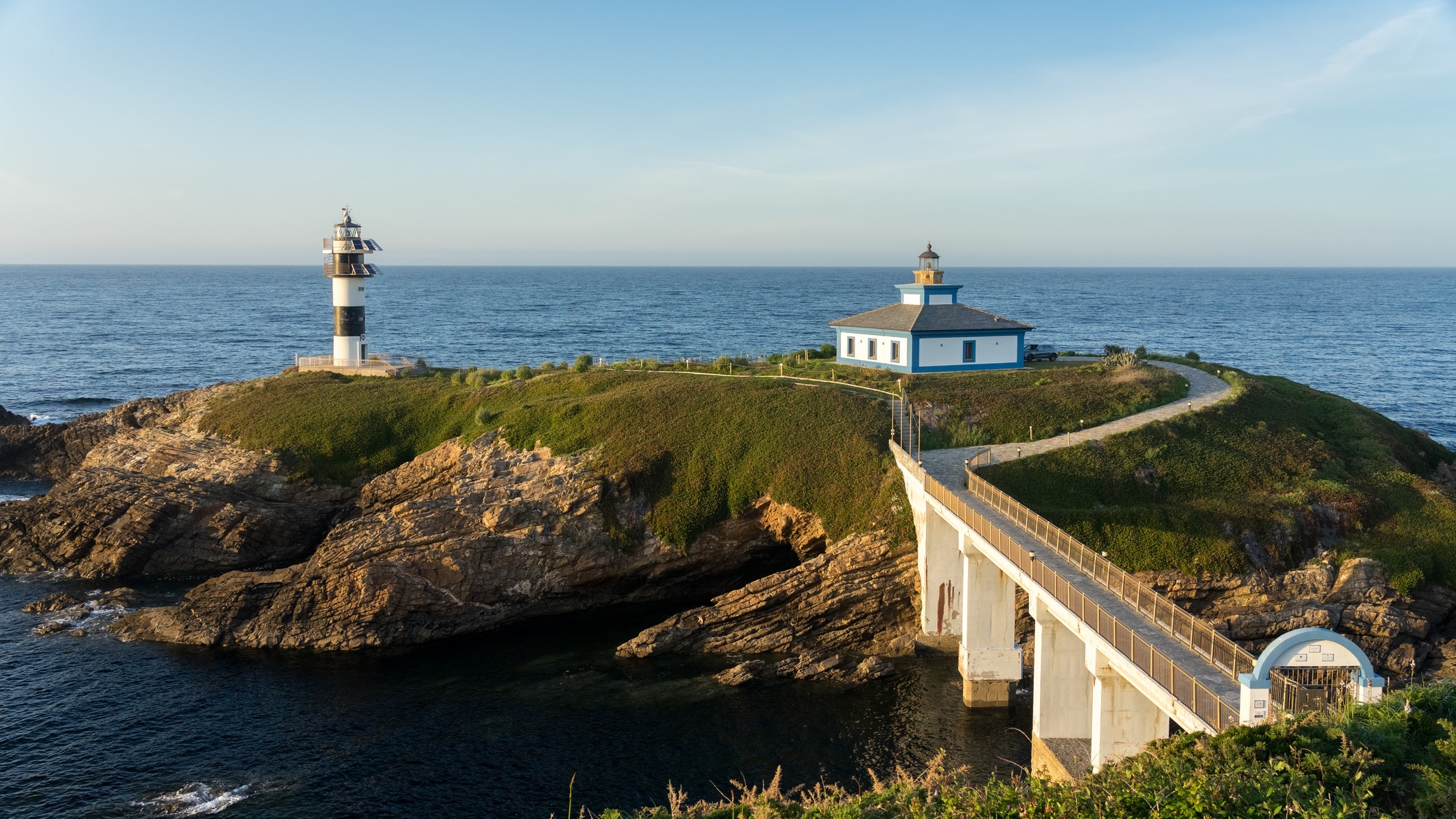 Faro de la Isla Pancha en Lugo, conectado por un puente a la costa. Edificio y torre blanca y negra junto al mar.