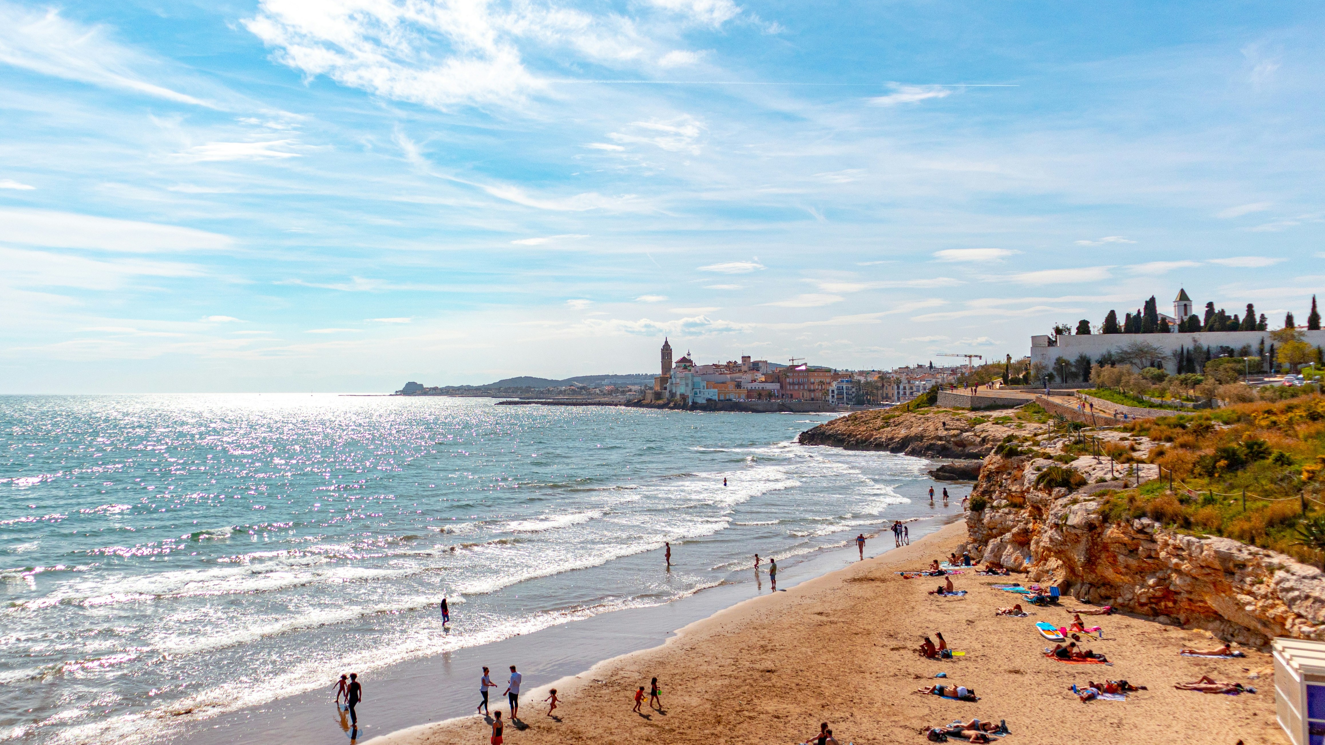 Vista costera de Sitges con casas junto al mar y acantilados bañados por las olas.