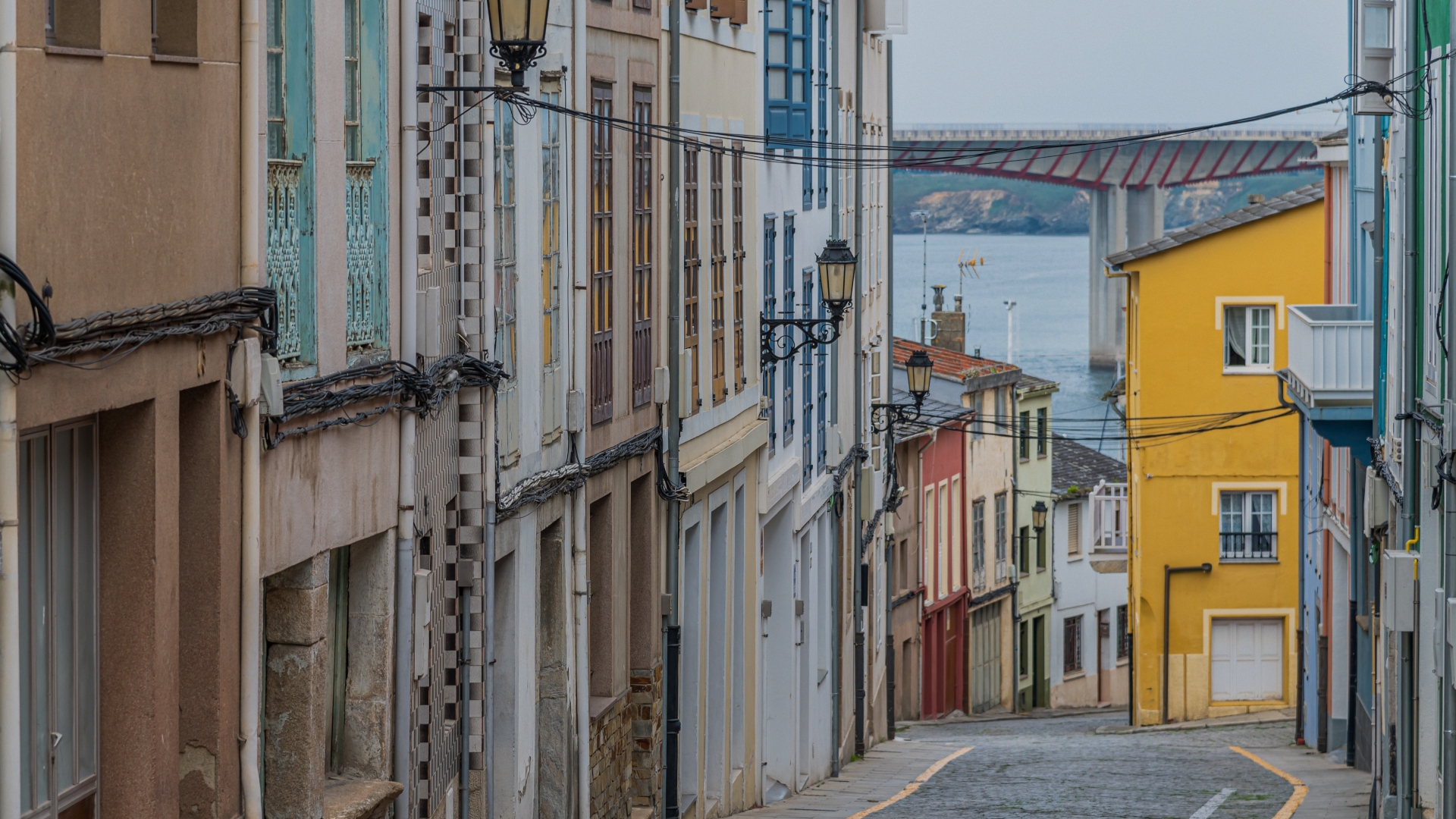 Calle del casco antiguo de Ribadeo con fachadas coloridas, vistas al mar Cantábrico y al puente de los Santos al fondo.