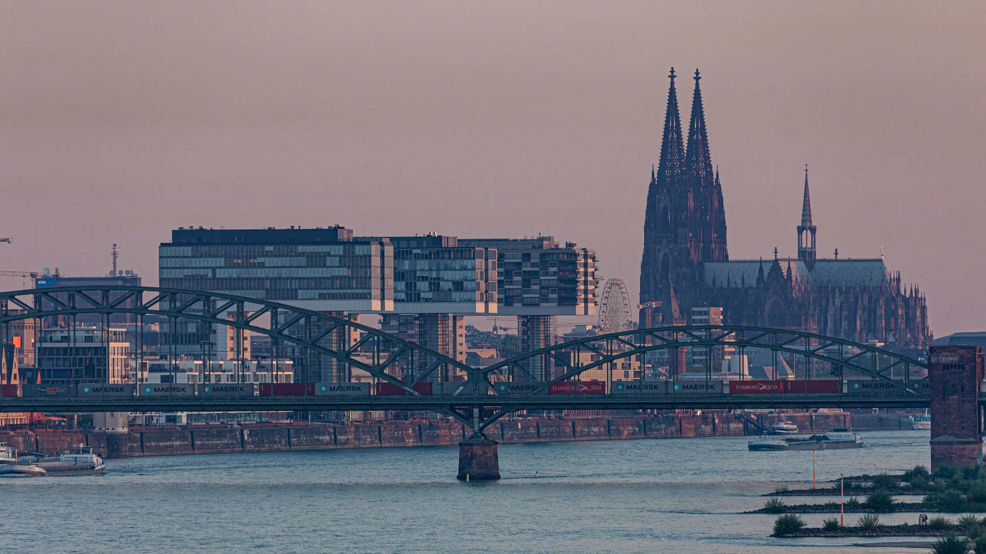  Skyline al atardecer en Colonia con el puente de Hohenzollern, edificios modernos y la silueta de la Catedral.