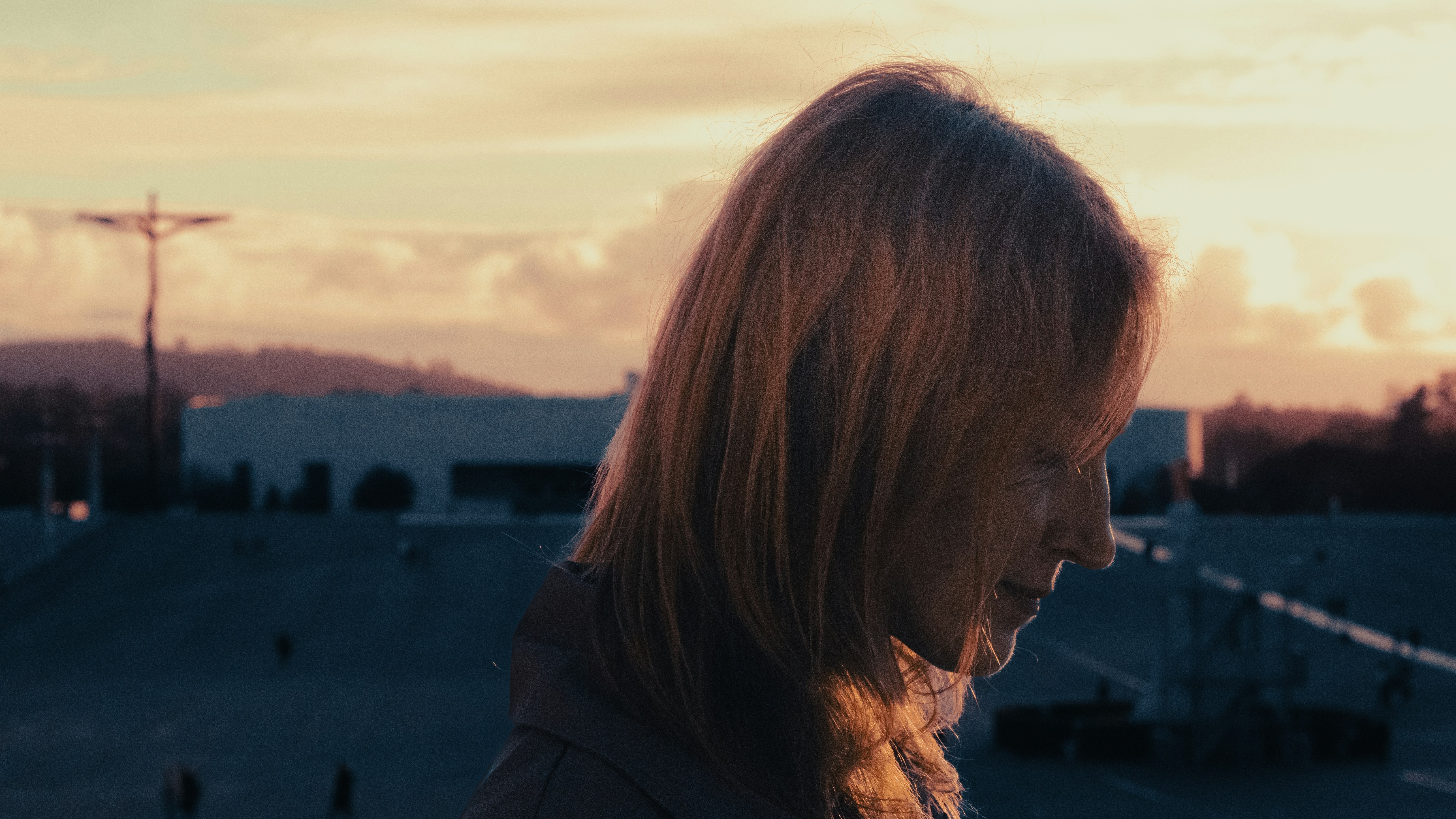 Mujer con cabello rojizo al atardecer en el Santuario de Fátima, silueta de la cruz y la Basílica de la Santísima Trinidad.