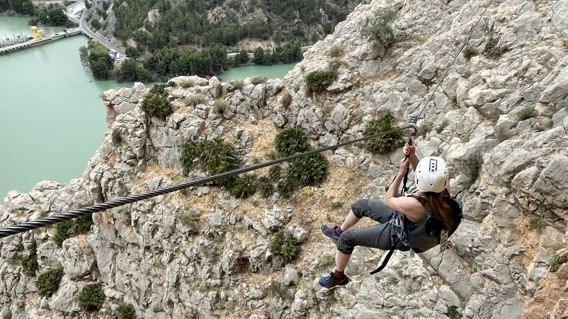 Persona descendiendo en tirolina sobre el embalse en la vía ferrata de El Chorro.