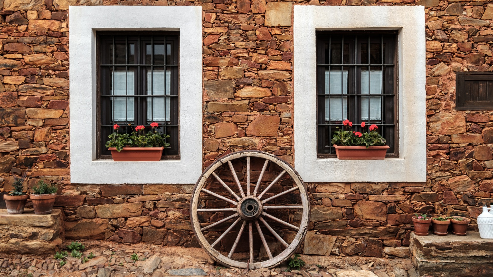 Fachada de casa maragata de piedra en Castrillo de los Polvazares, León, con una rueda de carro y dos ventanas.