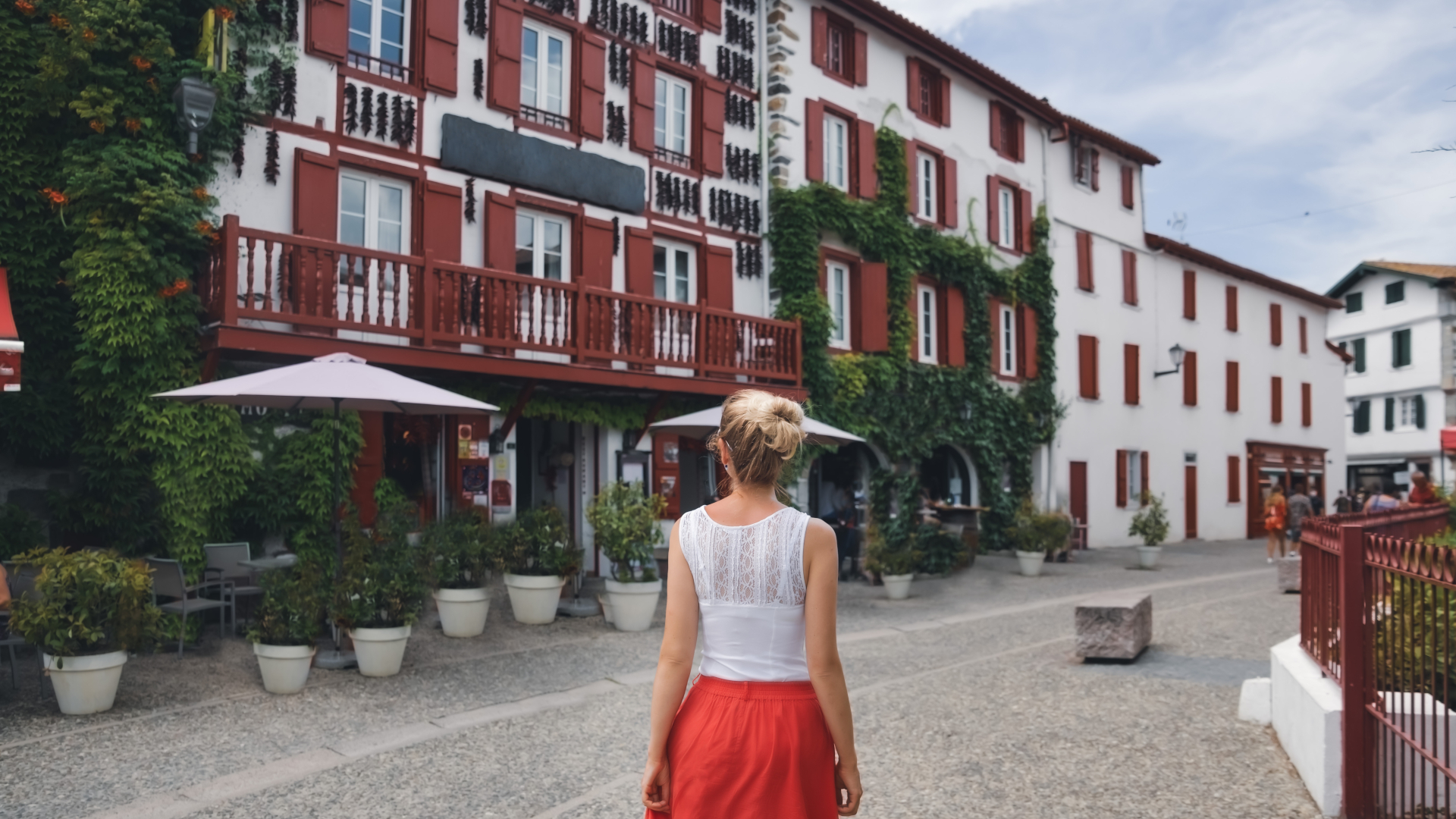 Mujer paseando entre casas con contraventanas rojas en Espelette, pueblo del País Vasco francés.