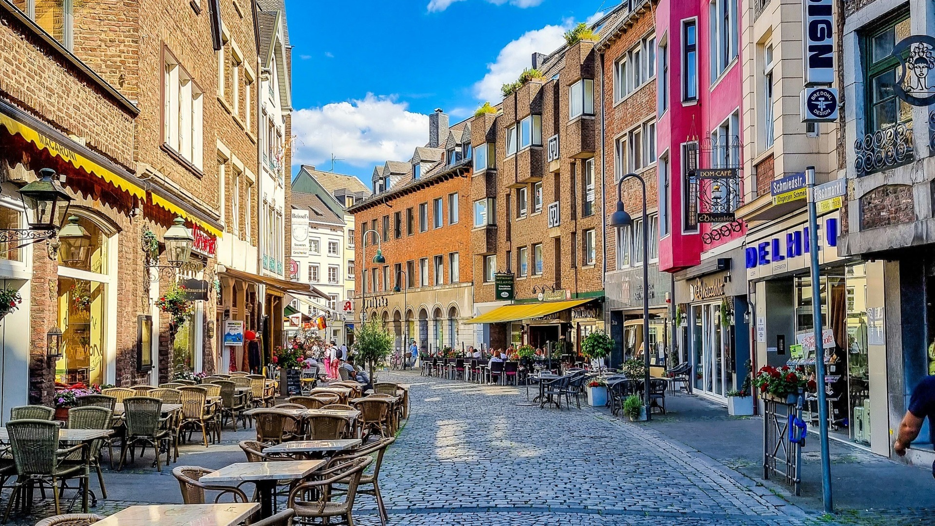  Terraza adoquinada con mesas de café rodeada de edificios históricos de ladrillo en Aquisgrán.
