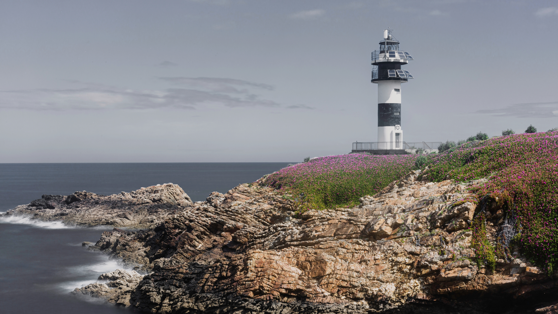 Faro de Isla Pancha en Ribadeo, sobre un acantilado cubierto de flores silvestres y con el mar Cantábrico al fondo.