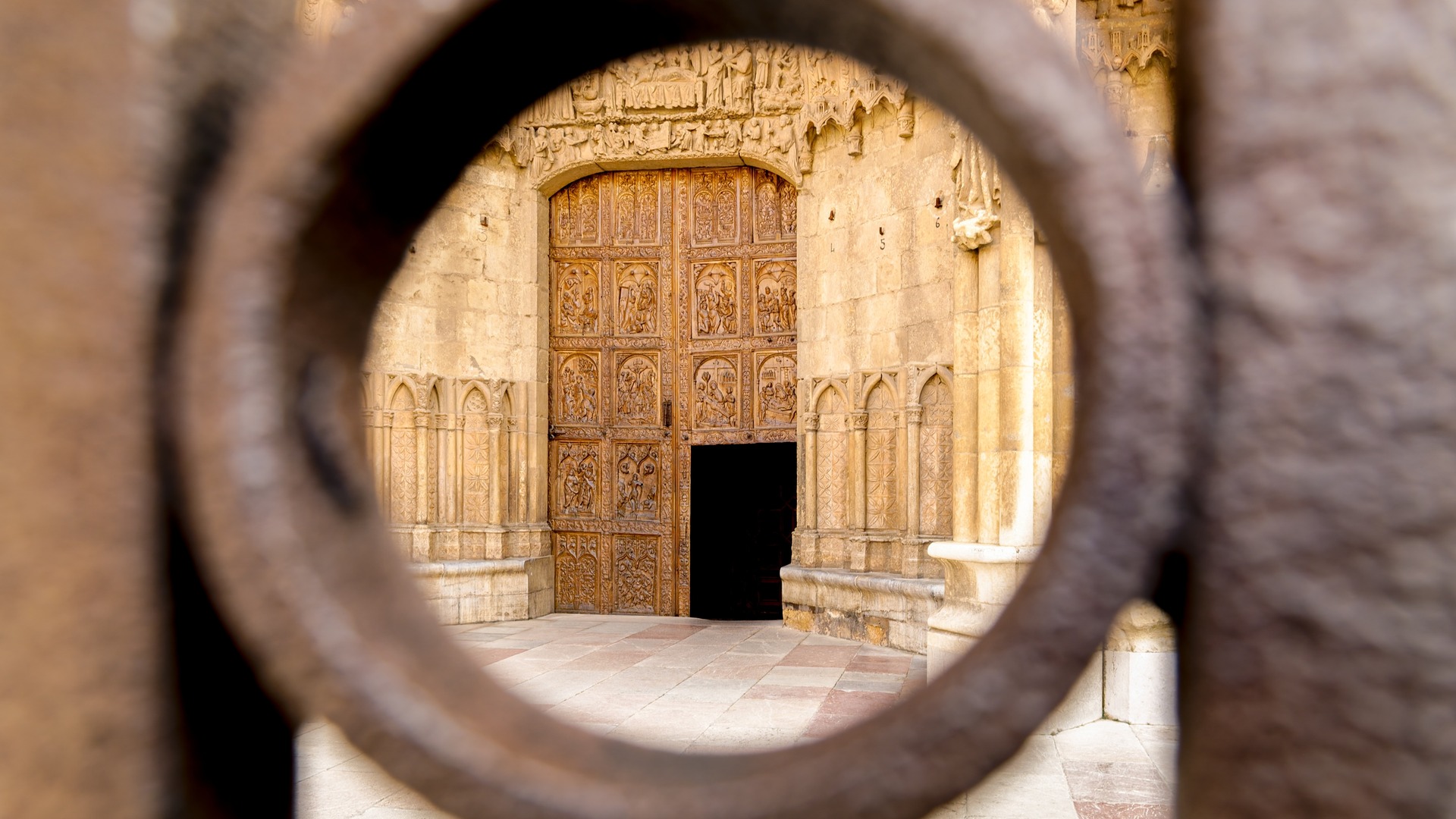 Puerta de madera tallada de la Catedral de León, estilo gótico, vista a través de una reja o mirilla de hierro forjado.