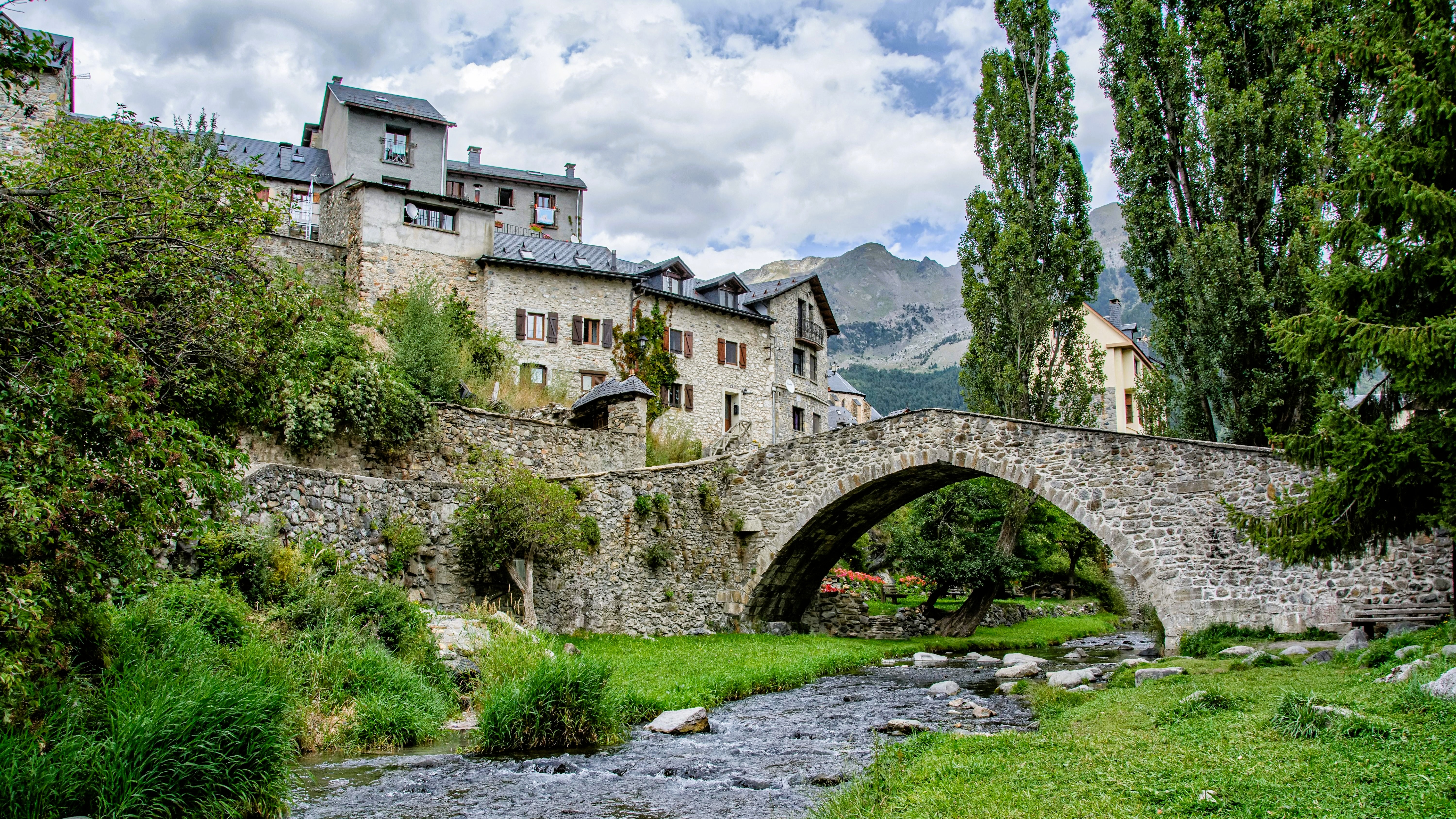 Puente de piedra sobre el río en Sallent de Gállego, con casas tradicionales pirenaicas y montaña de fondo, Huesca.