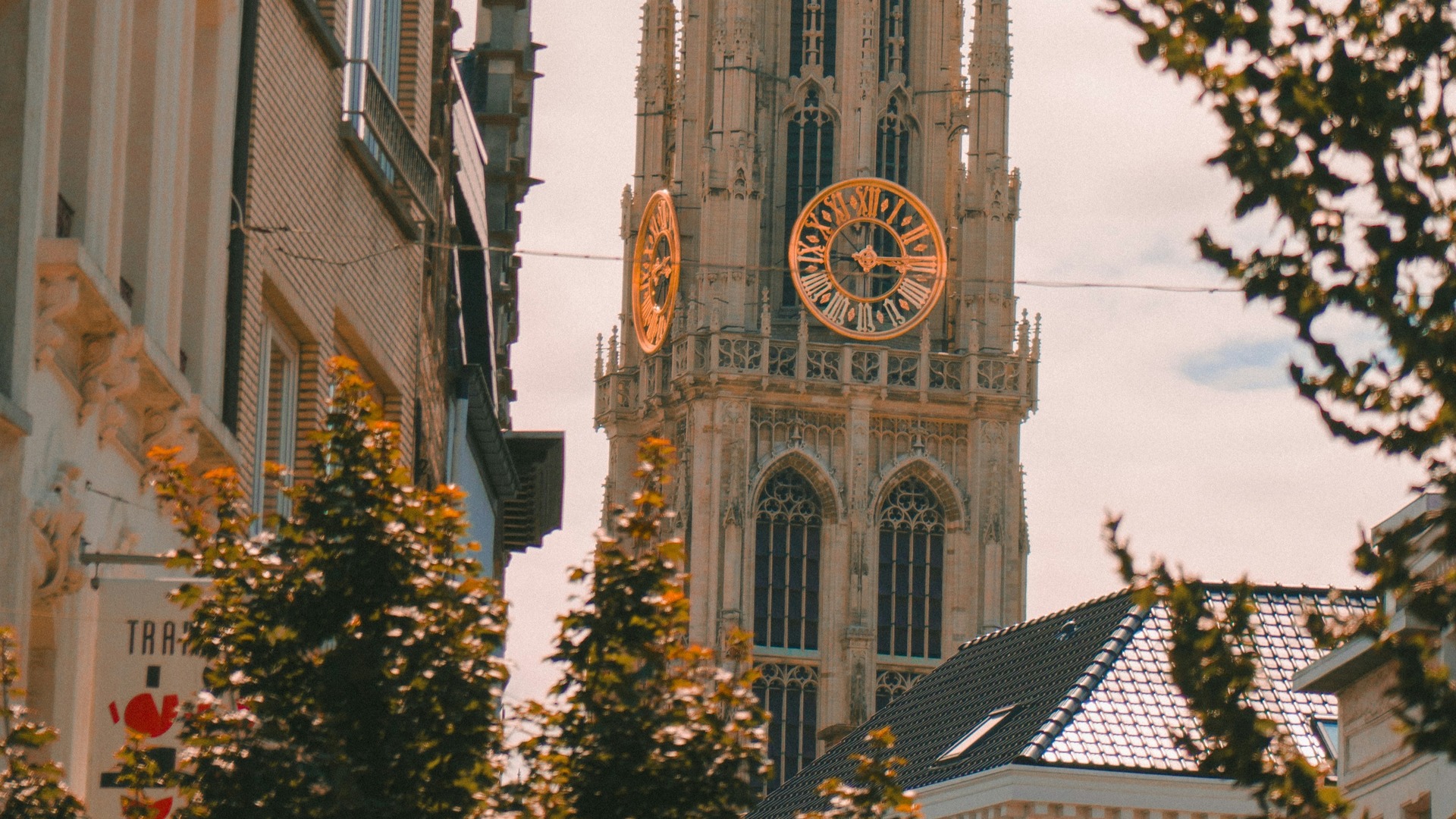 Torre de la Catedral de Nuestra Señora de Amberes, Bélgica, con sus grandes relojes dorados, vista entre edificios.