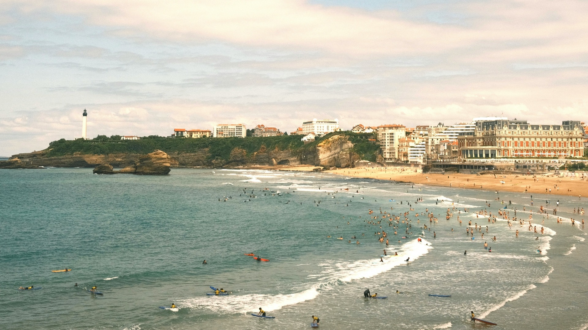 Playa de Biarritz con surfistas en el agua y edificios junto a la costa.