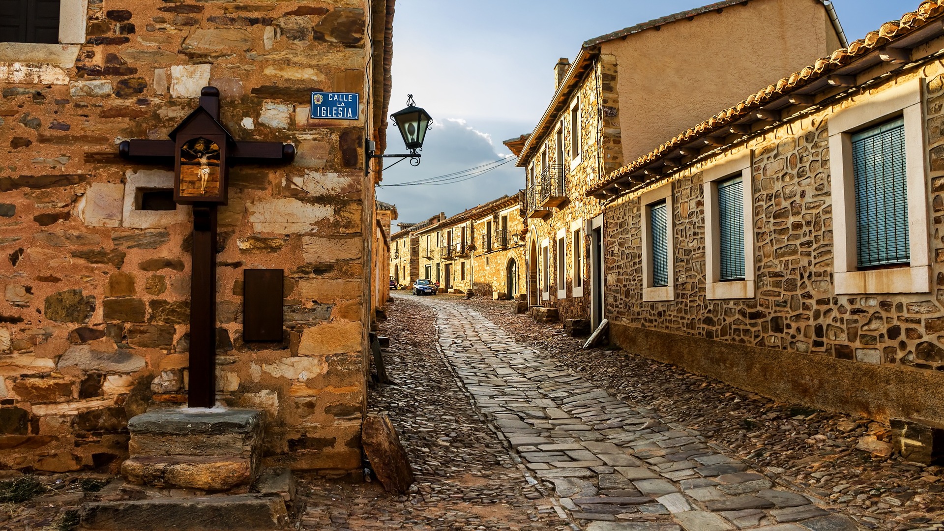 Calle empedrada tradicional en Castrillo de los Polvazares, León, con casas de piedra maragata y un crucero antiguo.