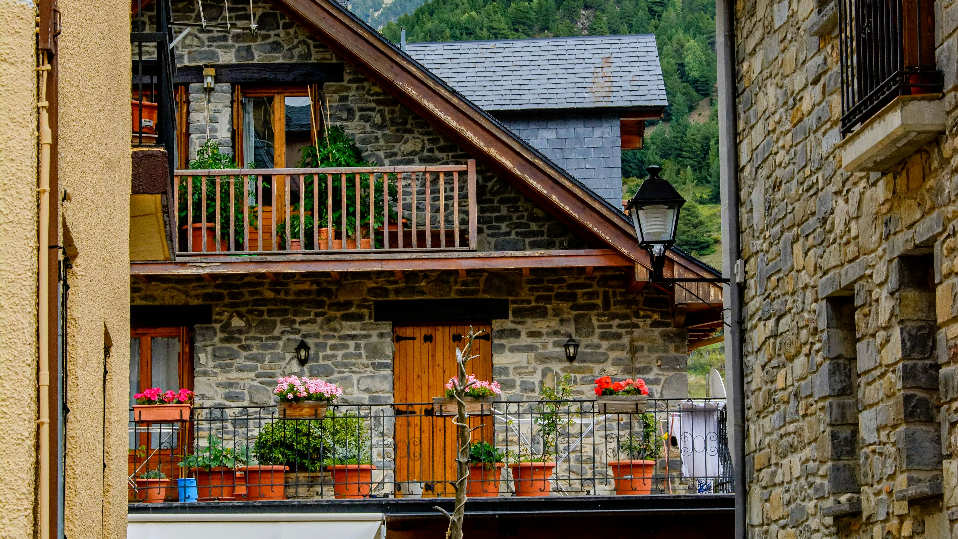 Fachada de casa de piedra tradicional en Jaca, Pirineo Aragonés, con balcones de madera decorados con macetas y flores.