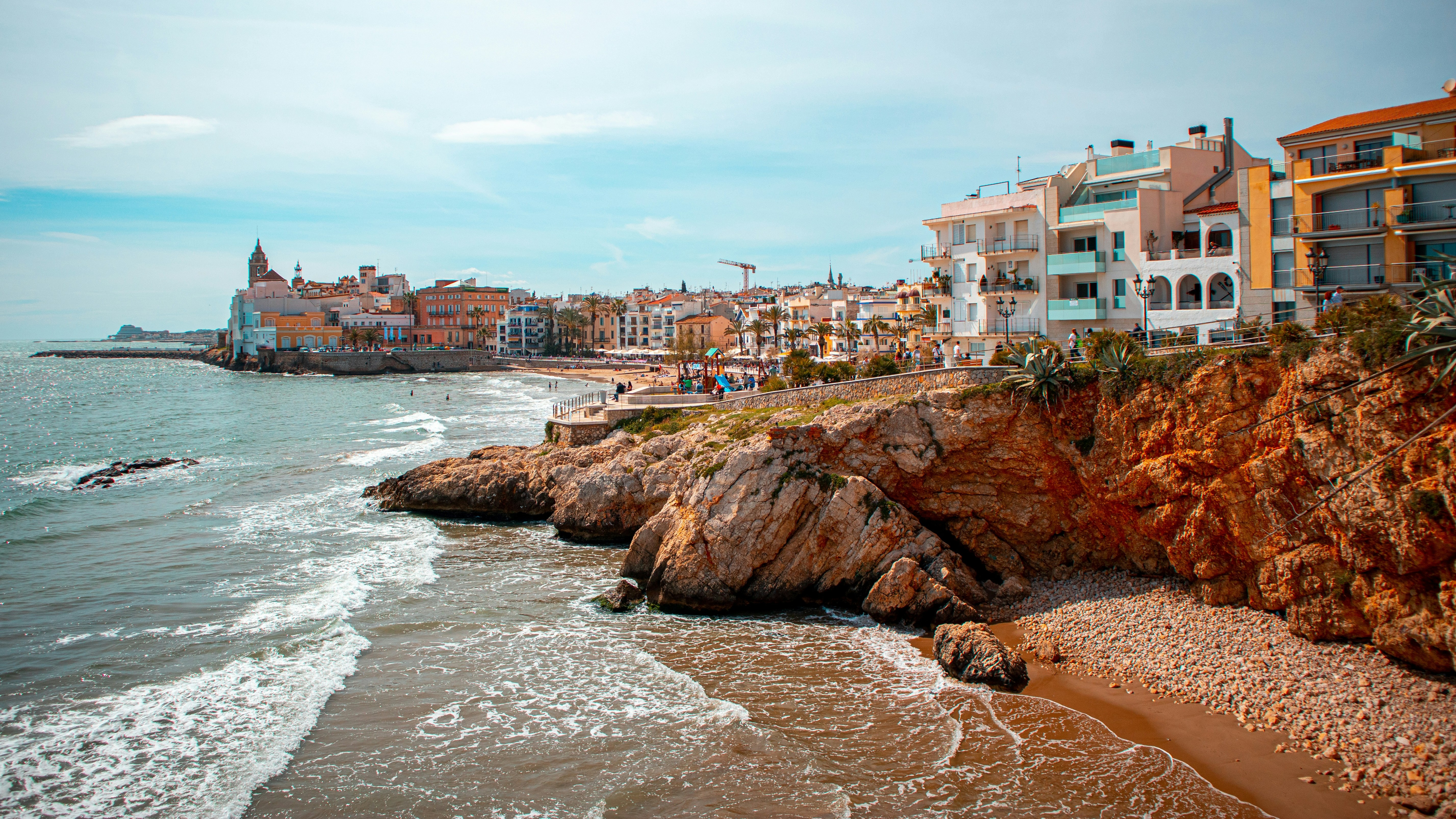 Vista costera de Sitges con casas junto al mar y acantilados bañados por las olas.