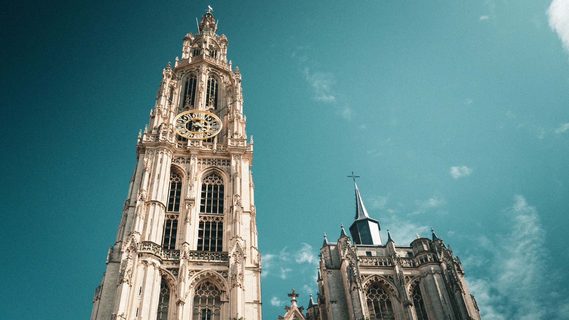 Torre gótica y fachada de la Catedral de Nuestra Señora de Amberes, Bélgica, con cielo azul turquesa dramático.
