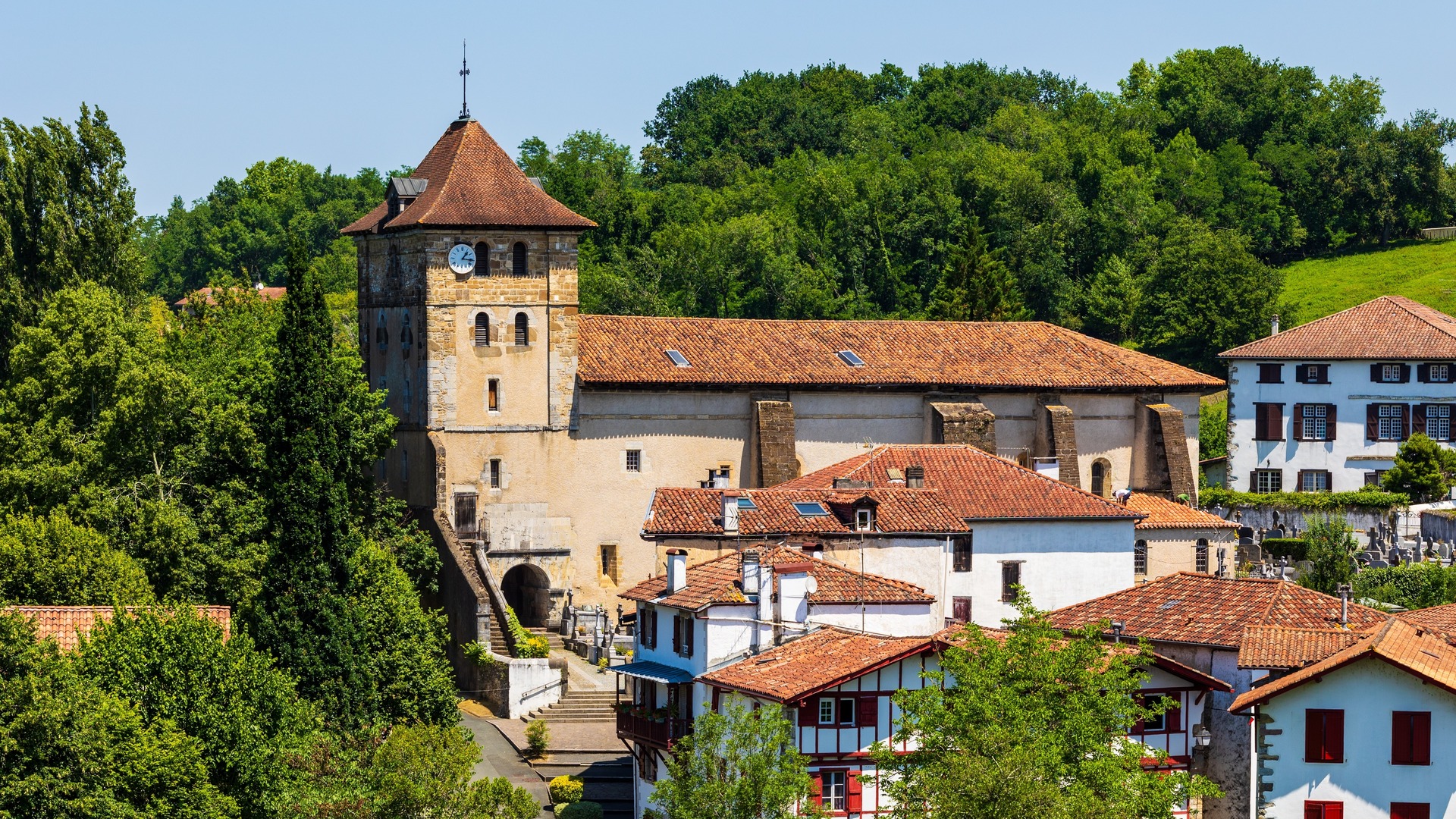 Iglesia de San Esteban rodeada de casas tradicionales blancas y bosque en el pueblo navarro de Bera.