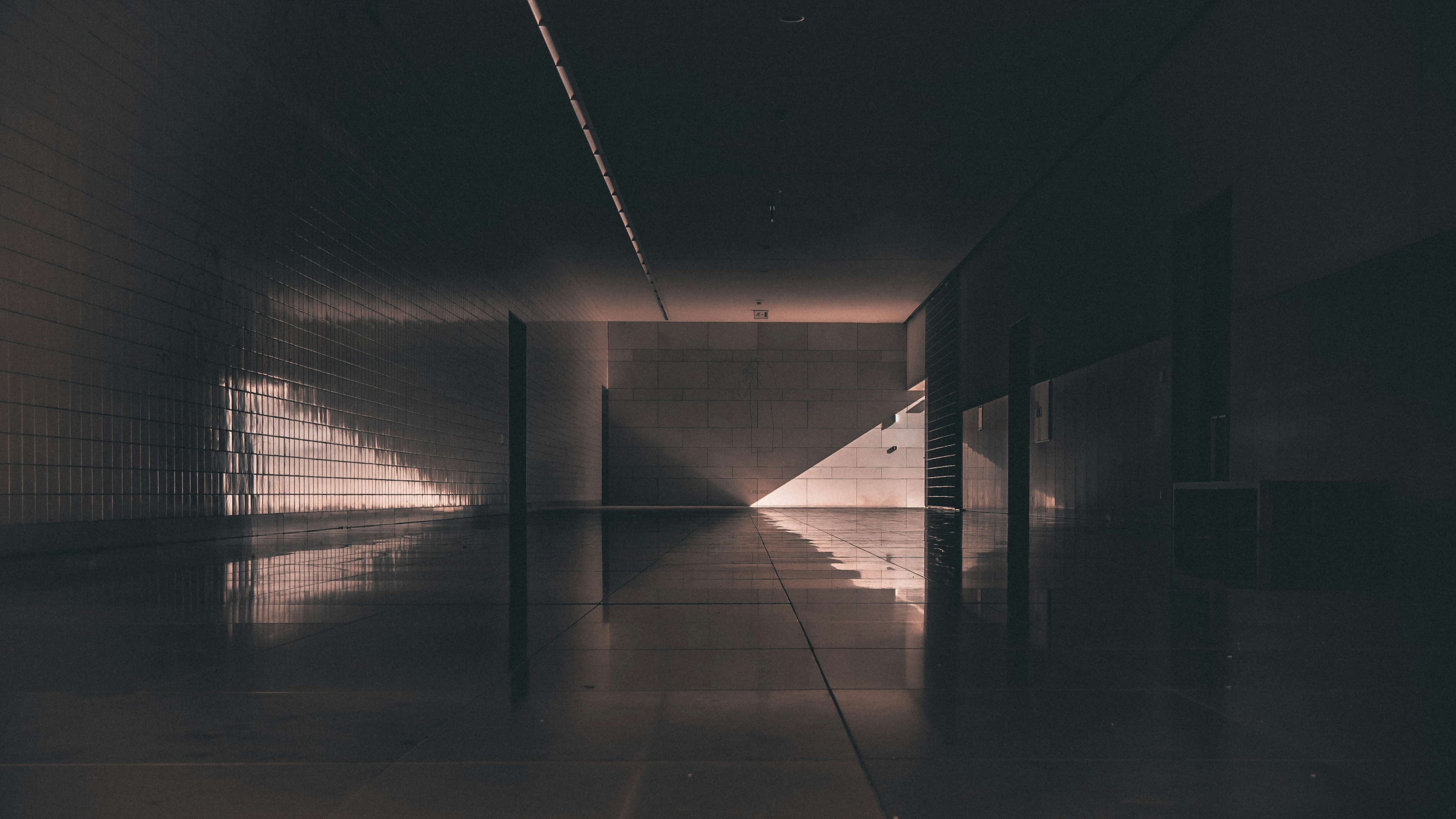 Pasillo interior oscuro en Fátima con suelo reflectante y un rayo de luz que irradia desde el fondo.