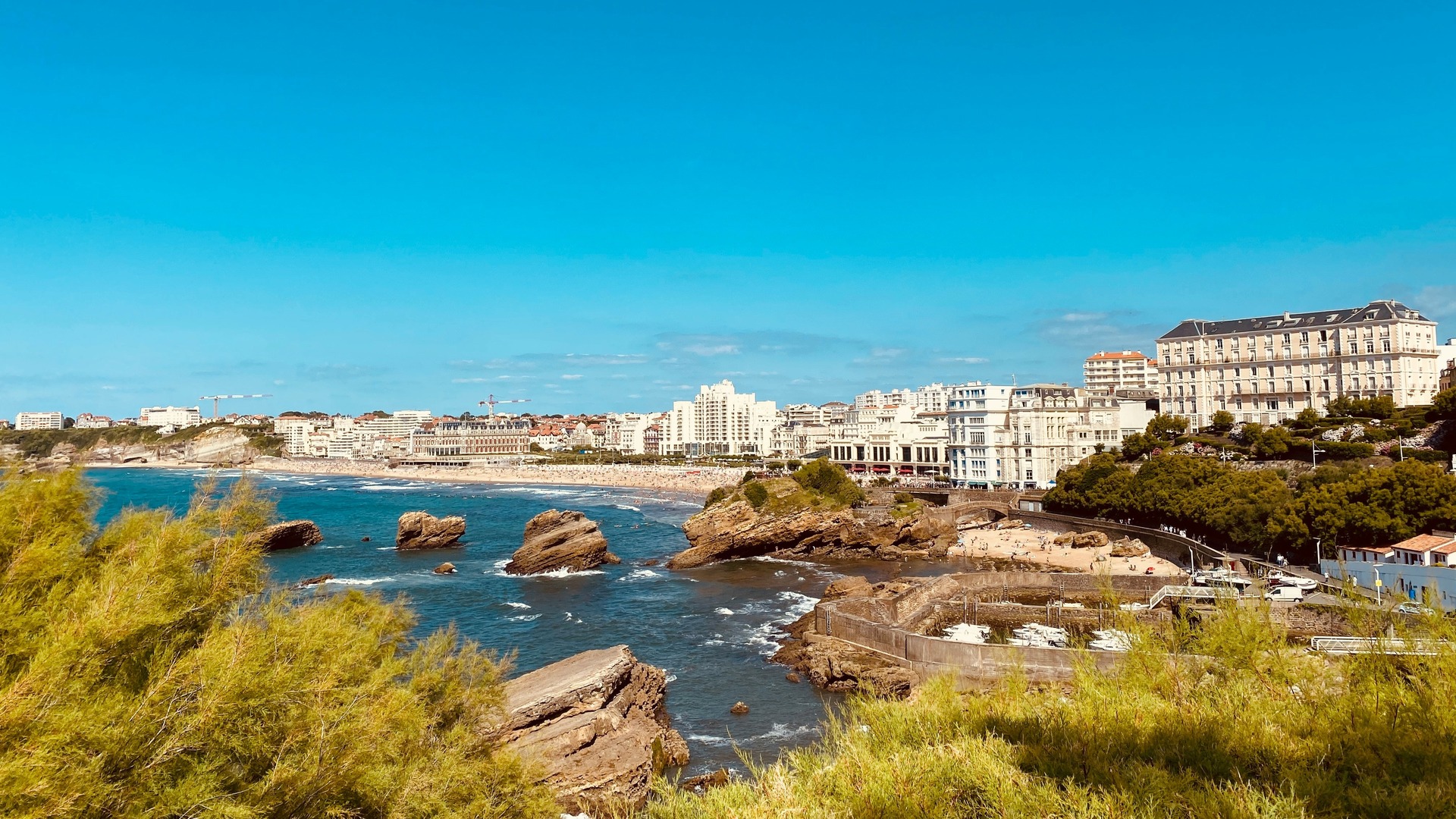 Vista costera de Biarritz con acantilados, playa y edificios junto al mar.
