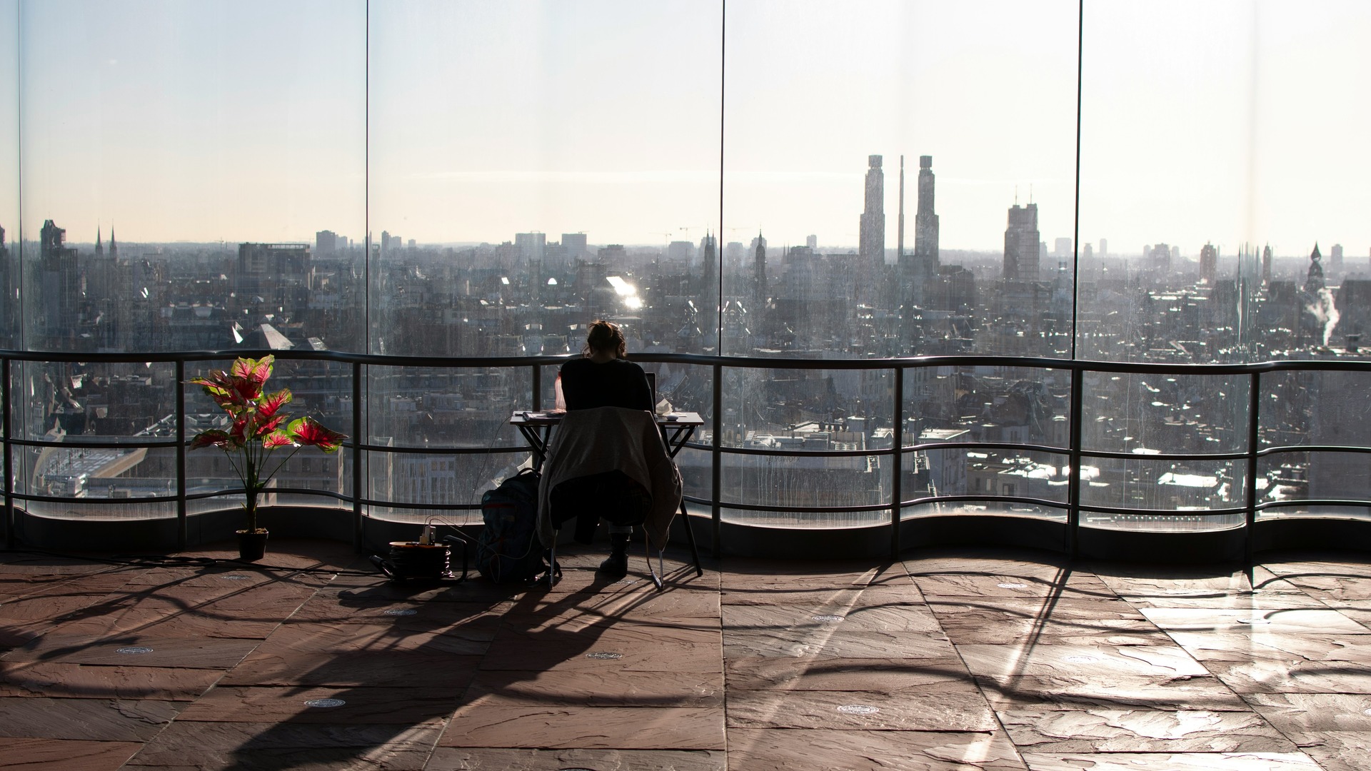 Persona trabajando en terraza con vistas panorámicas del skyline de Amberes, Bélgica, con edificios y torres altas.