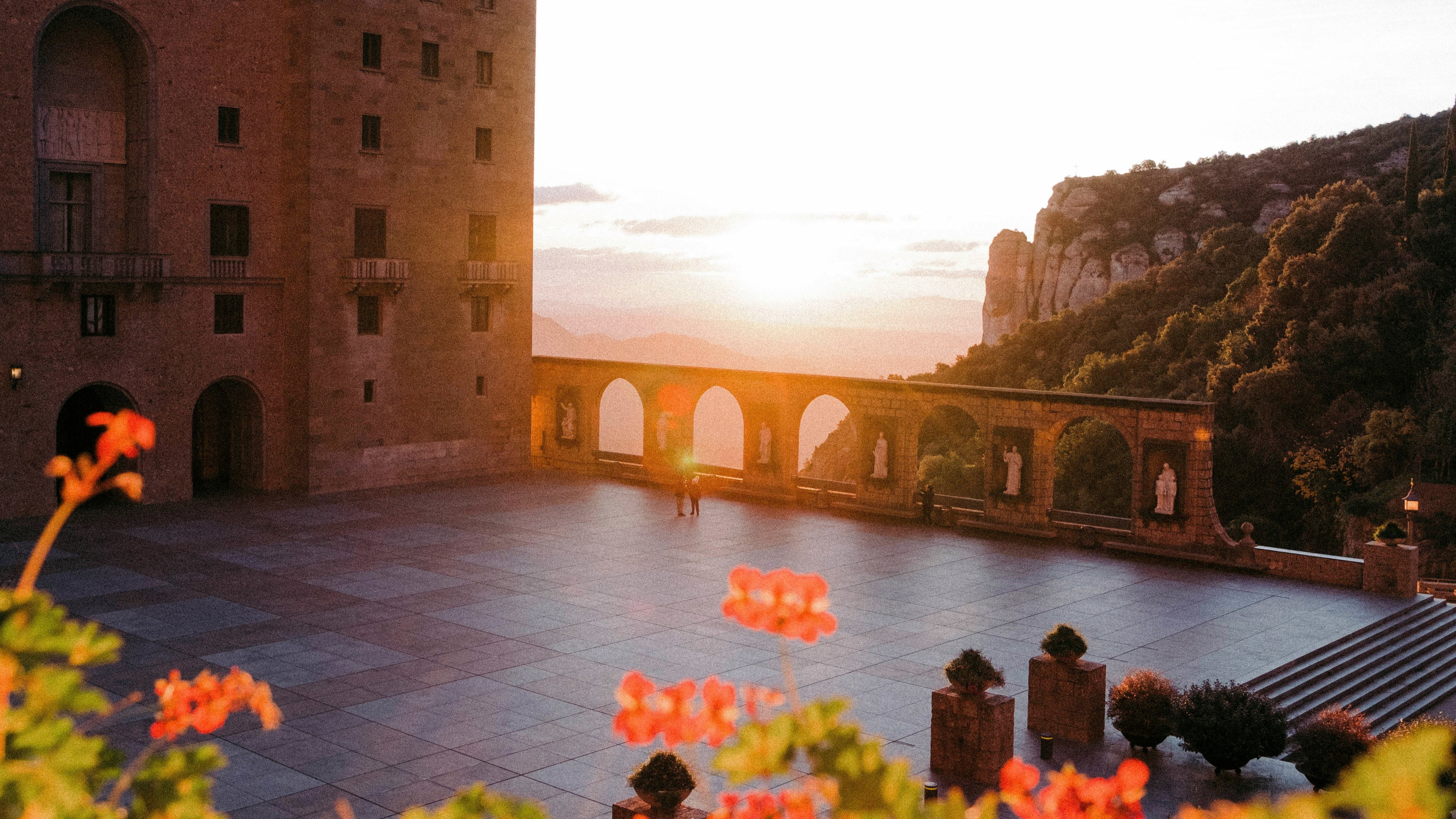Patio del monasterio de Montserrat al atardecer, con arcos y montañas al fondo.