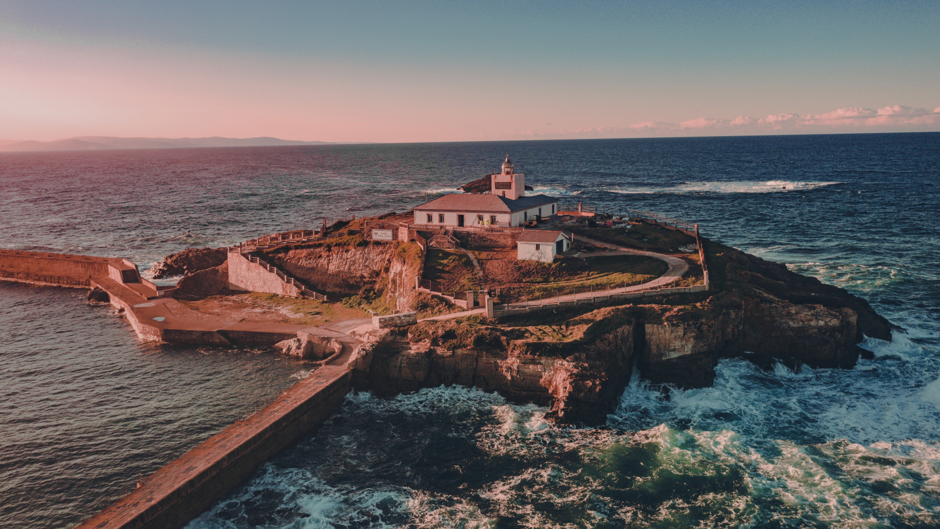 Vista aérea del faro de Tapia de Casariego al atardecer, rodeado por el mar Cantábrico y los acantilados de la costa asturiana.