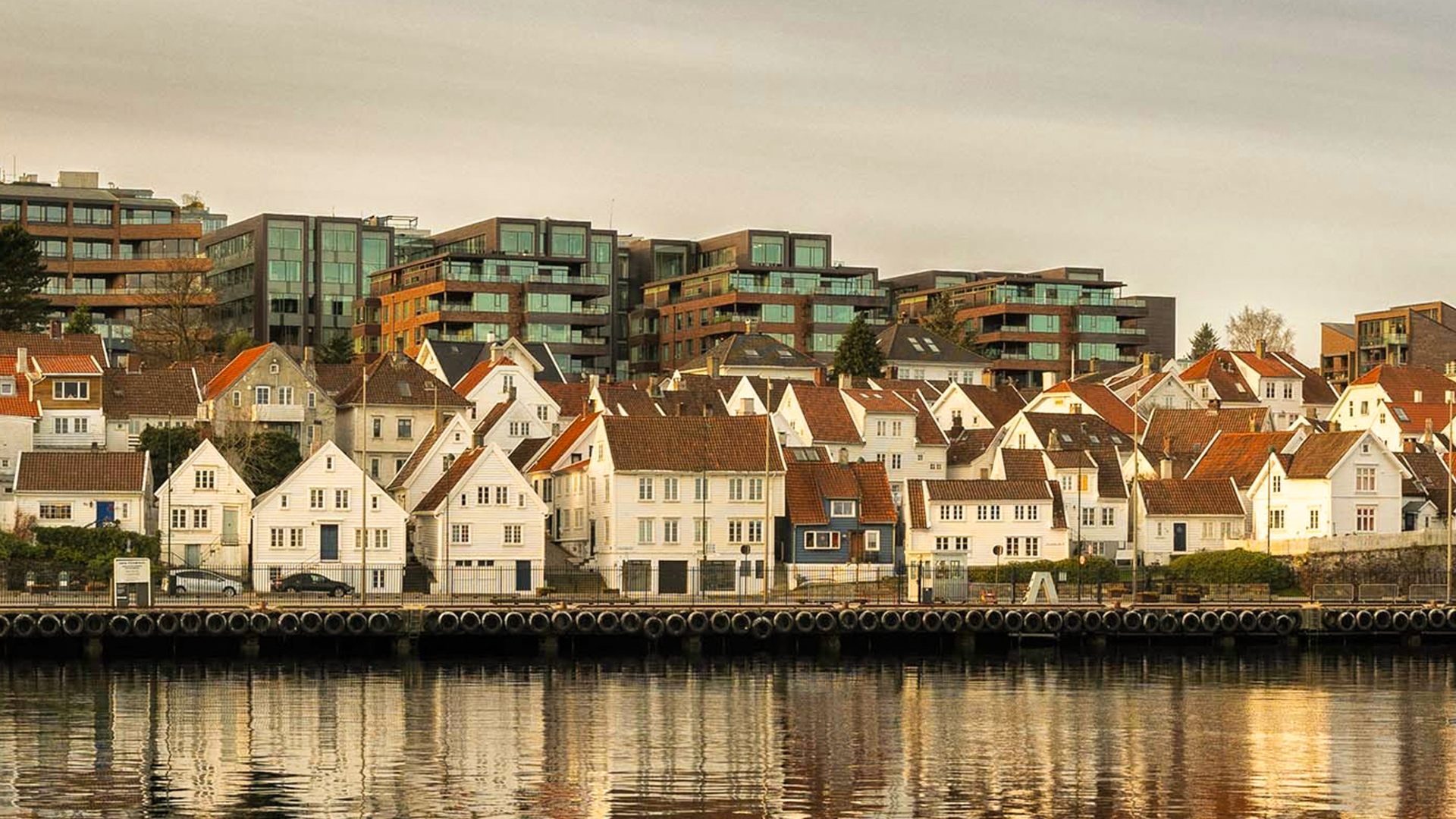 Casas tradicionales de madera en Stavanger, Noruega, frente al puerto con reflejos dorados al atardecer.