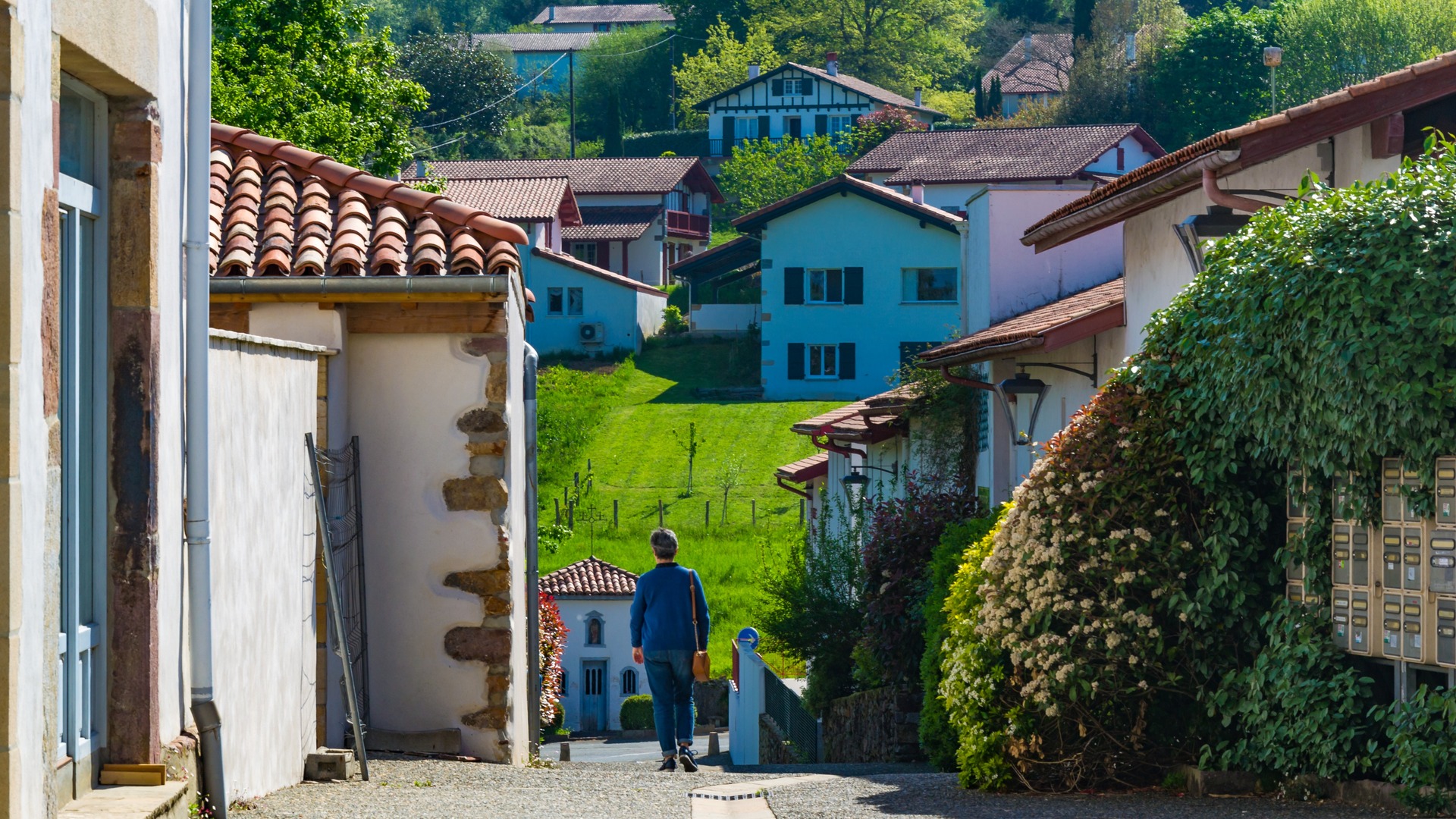 Persona caminando entre casas blancas y verdes prados en Ainhoa, en el País Vasco francés.