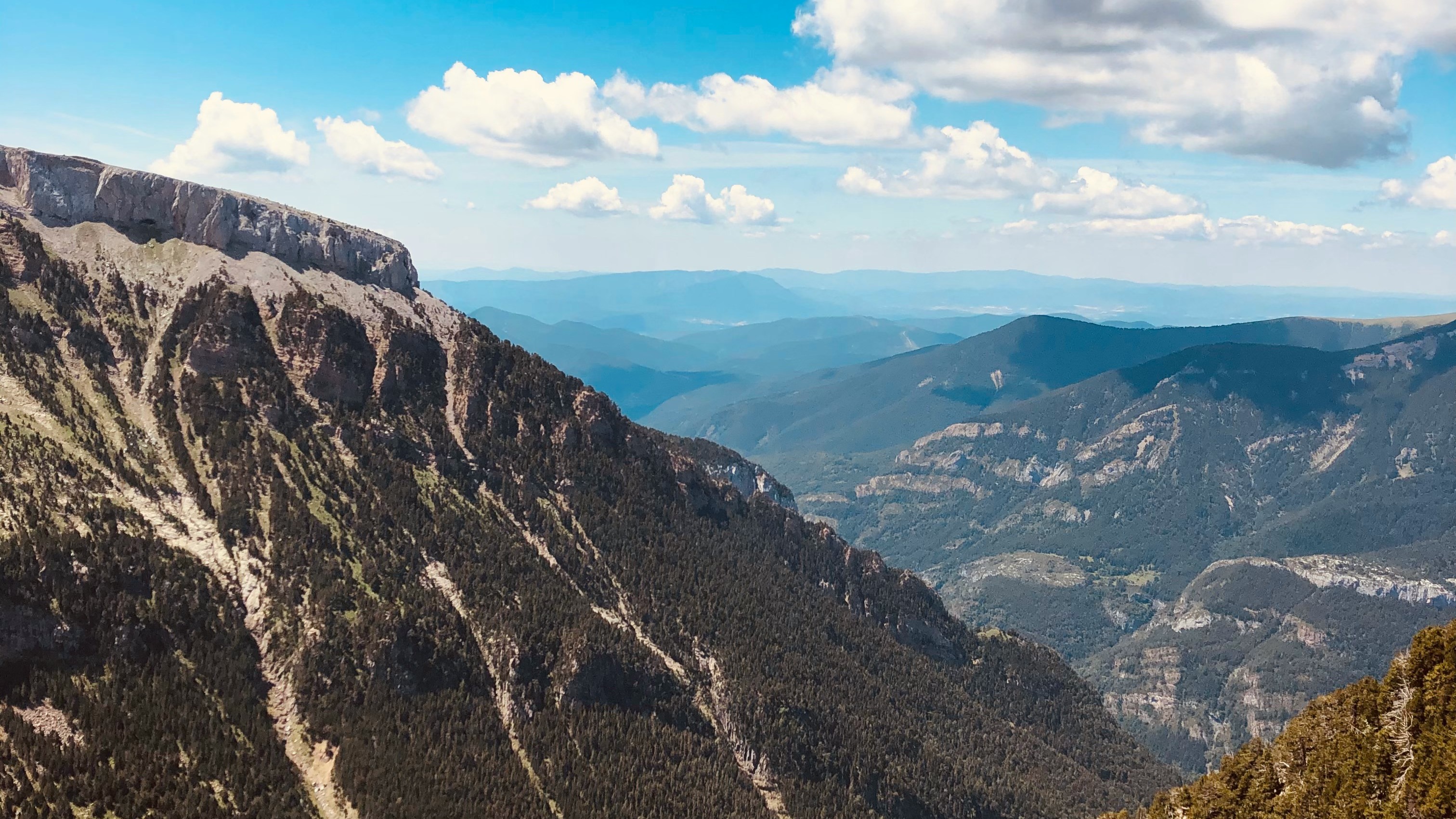 Vistas panorámicas del Valle de Canfranc, Pirineo Aragonés, con laderas boscosas y picos bajo un cielo azul con nubes.