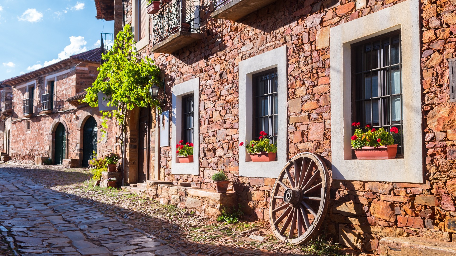 Calle empedrada de Castrillo de los Polvazares, León, con fachadas de piedra maragata y rueda de carro decorativa.