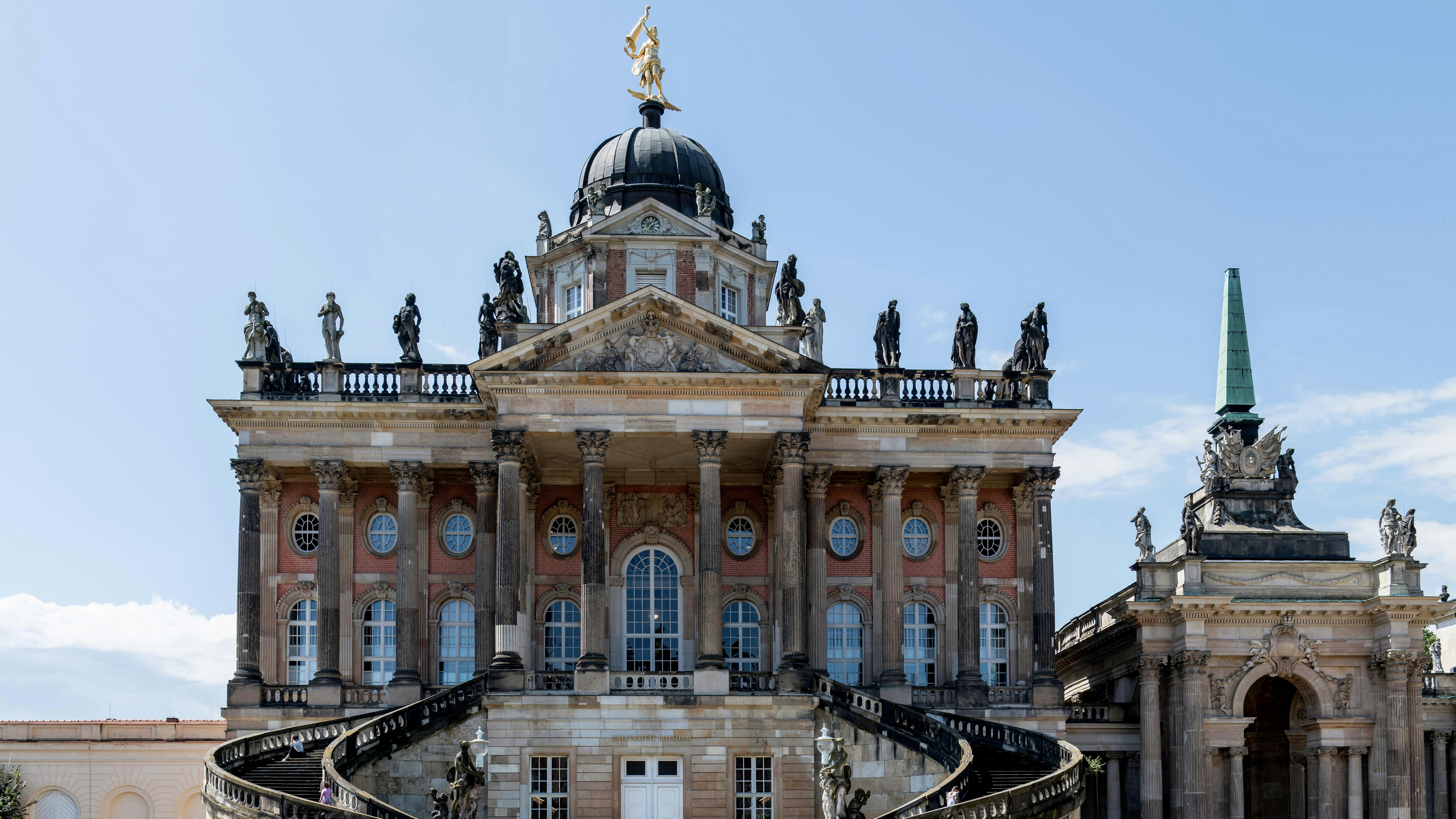 Fachada y escalinata principal del Nuevo Palacio (Neues Palais) en Potsdam, con estatuas y cúpula barroca.