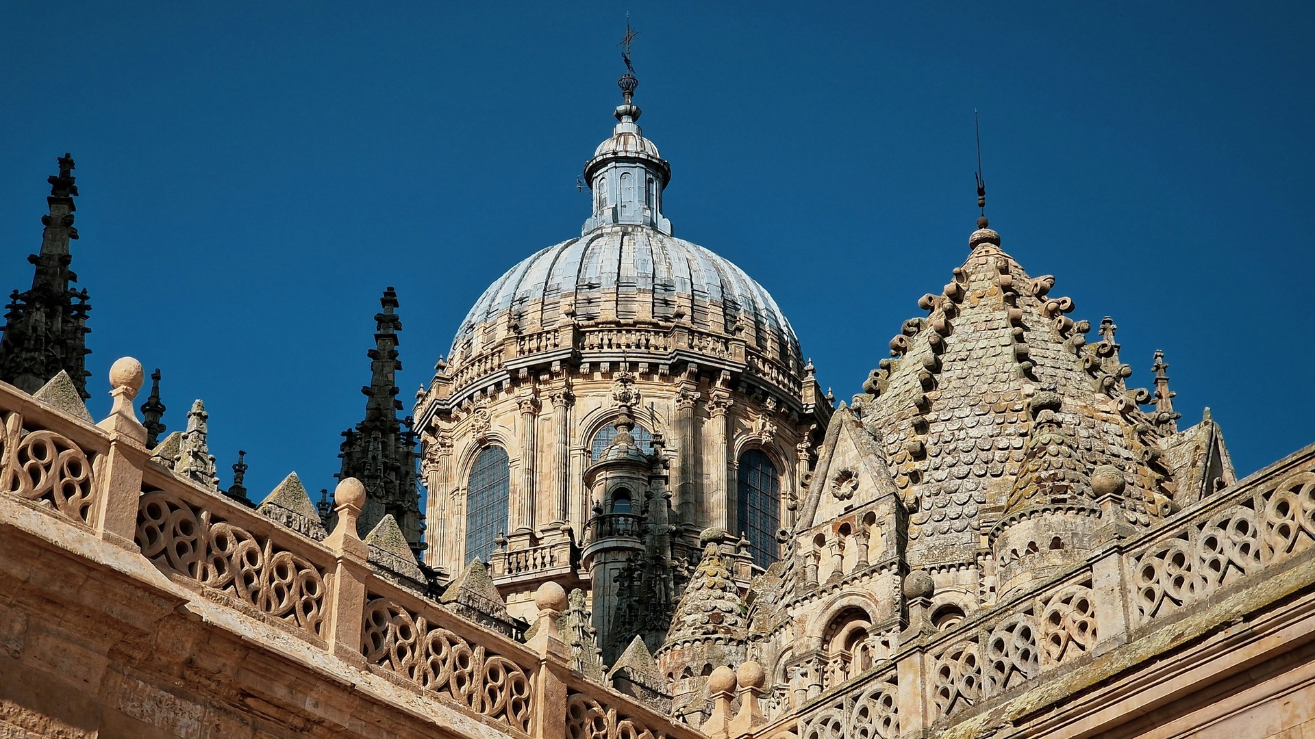 Detalle de las cúpulas y la balaustrada gótica de la Catedral Nueva de Salamanca, España, bajo un cielo azul intenso.
