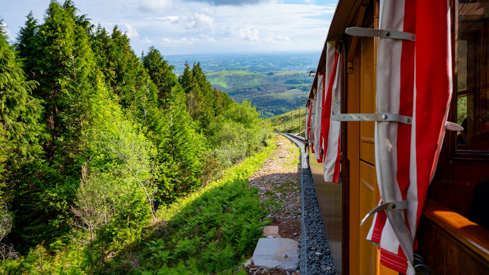 Tren de la Rhune avanzando entre bosques, con vistas al valle desde la montaña en la zona de Ainhoa.