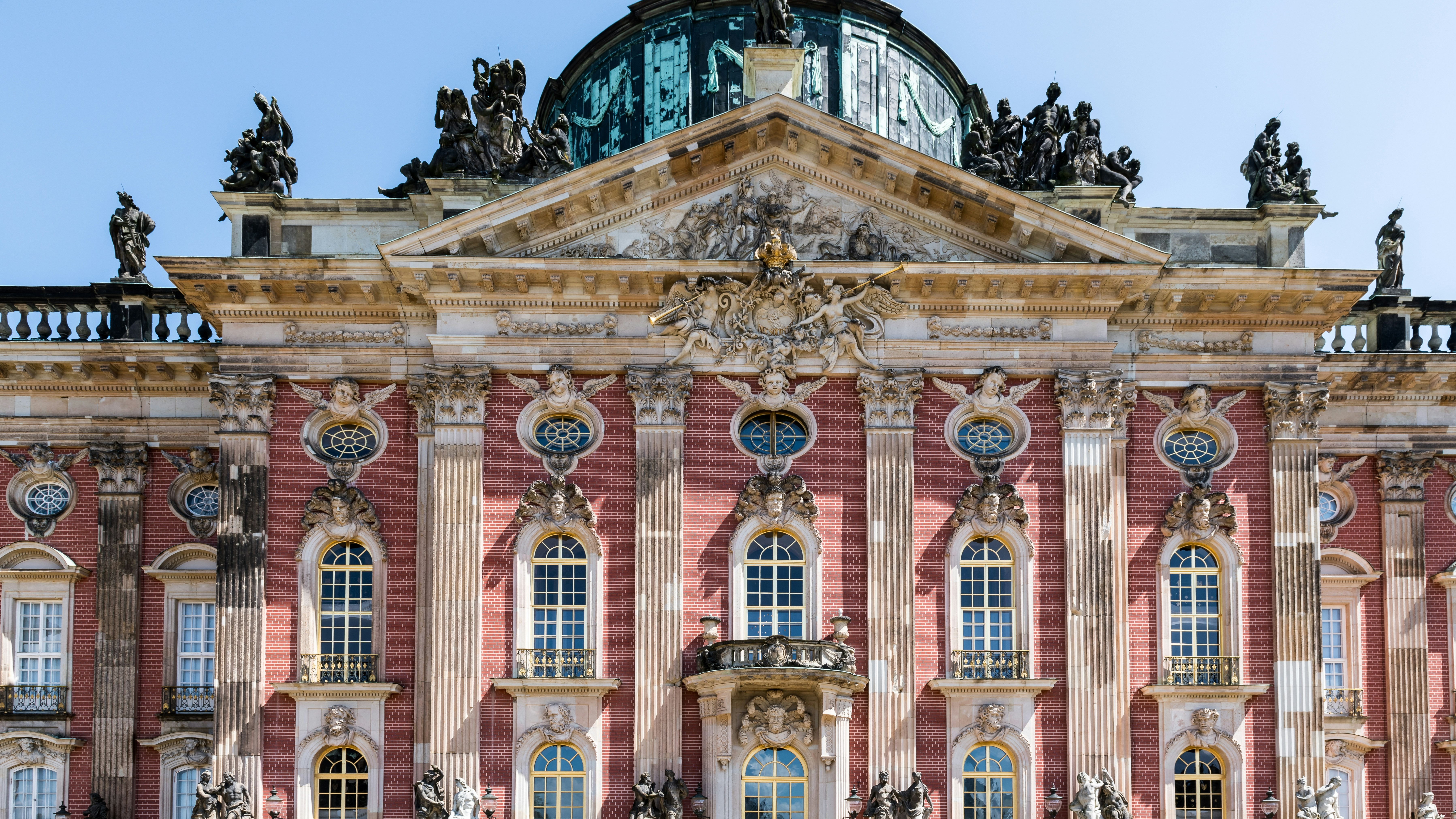 Fachada principal del Detalle de la fachada barroca del Nuevo Palacio (Neues Palais) en Potsdam, con ladrillo rojo, estatuas y cúpula.