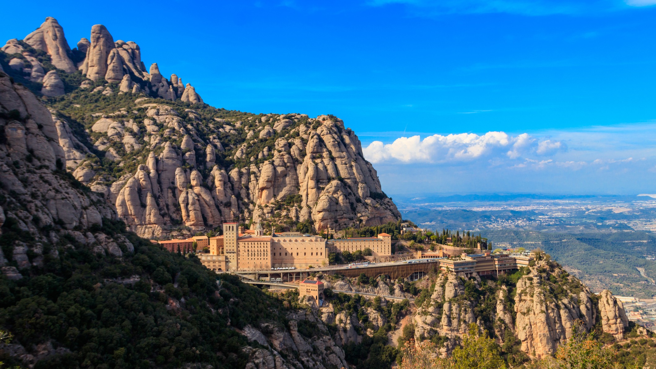 Monasterio de Montserrat rodeado de montañas rocosas bajo cielo azul.