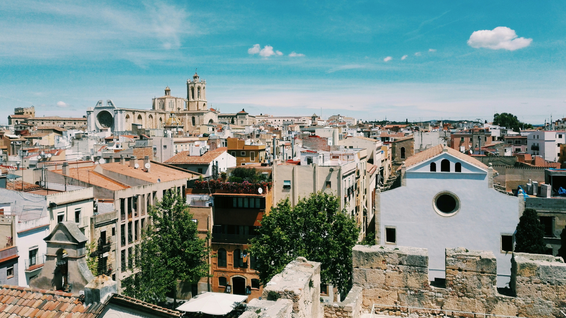Vista panorámica de Tarragona desde lo alto, con la Catedral en el horizonte y tejados ocres bajo un cielo azul.